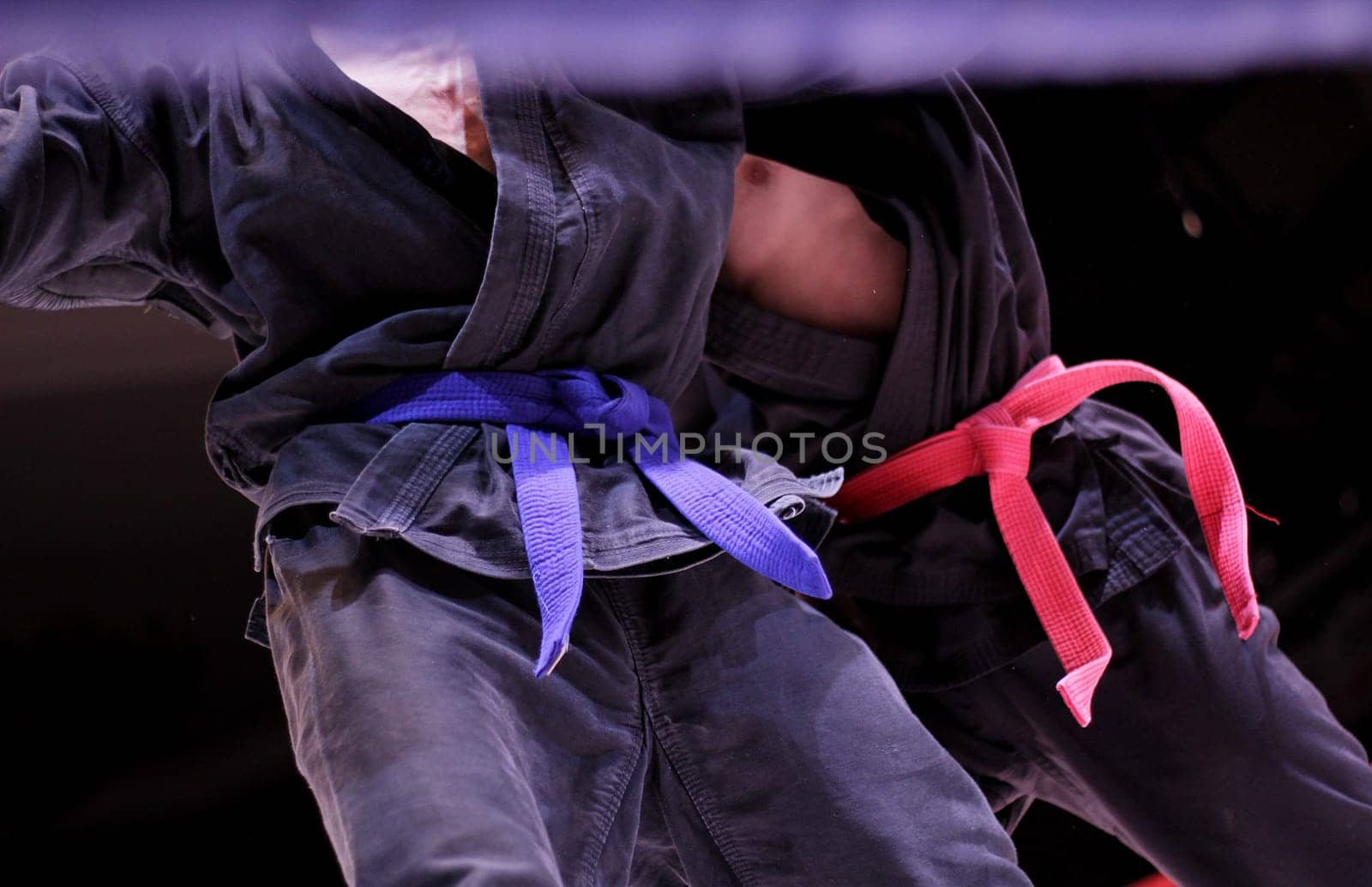 Man in dark kimono and blue belt training karate over dark background. 2 belts red and blue. Kimono for martial arts, sportswear, martial arts apparel
