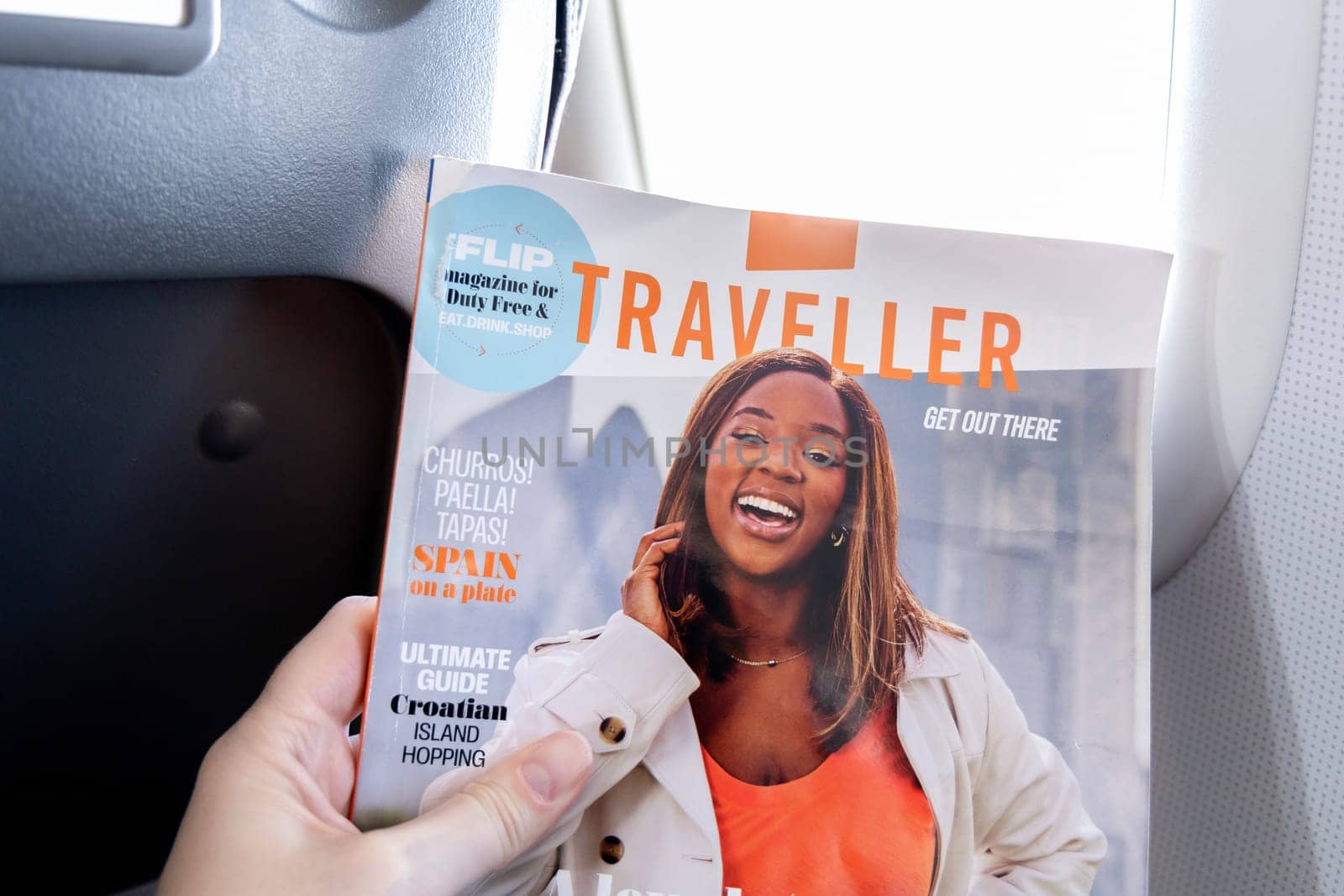 Female hands holding the magazine Traveller on board an airplane. Paris, France - January 6, 2025