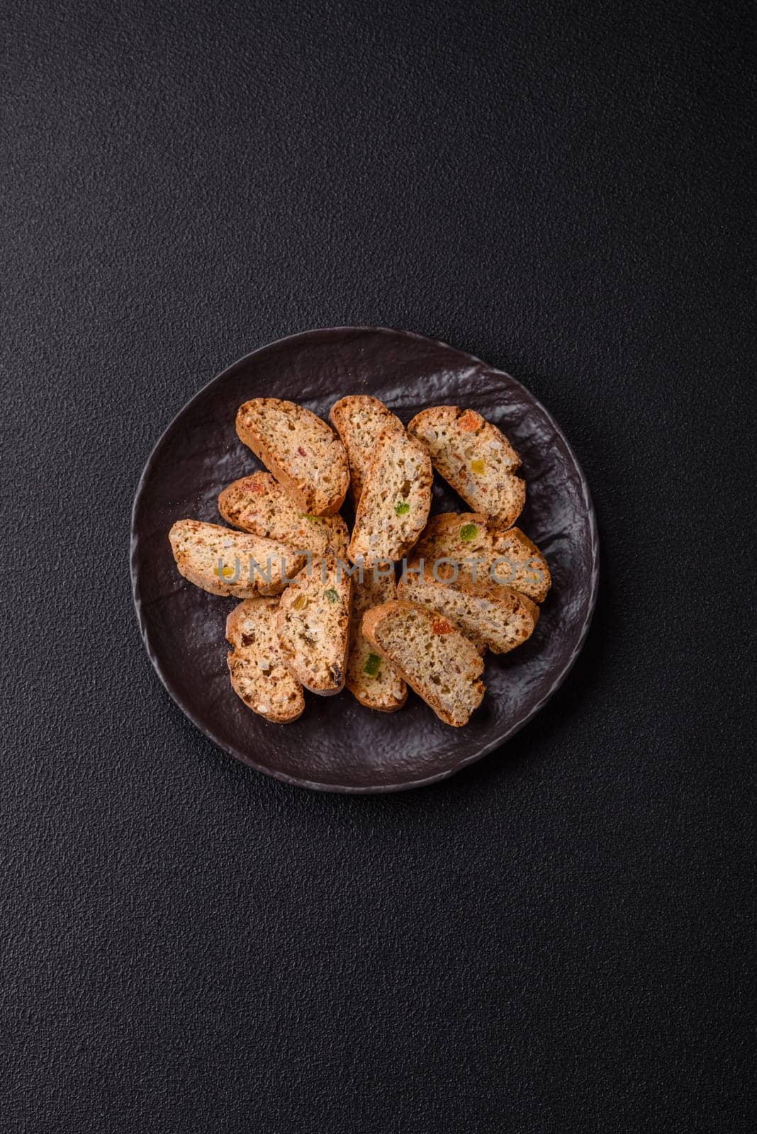 Freshly baked Italian cantuccini cookies with nuts and candied fruits on dark concrete background