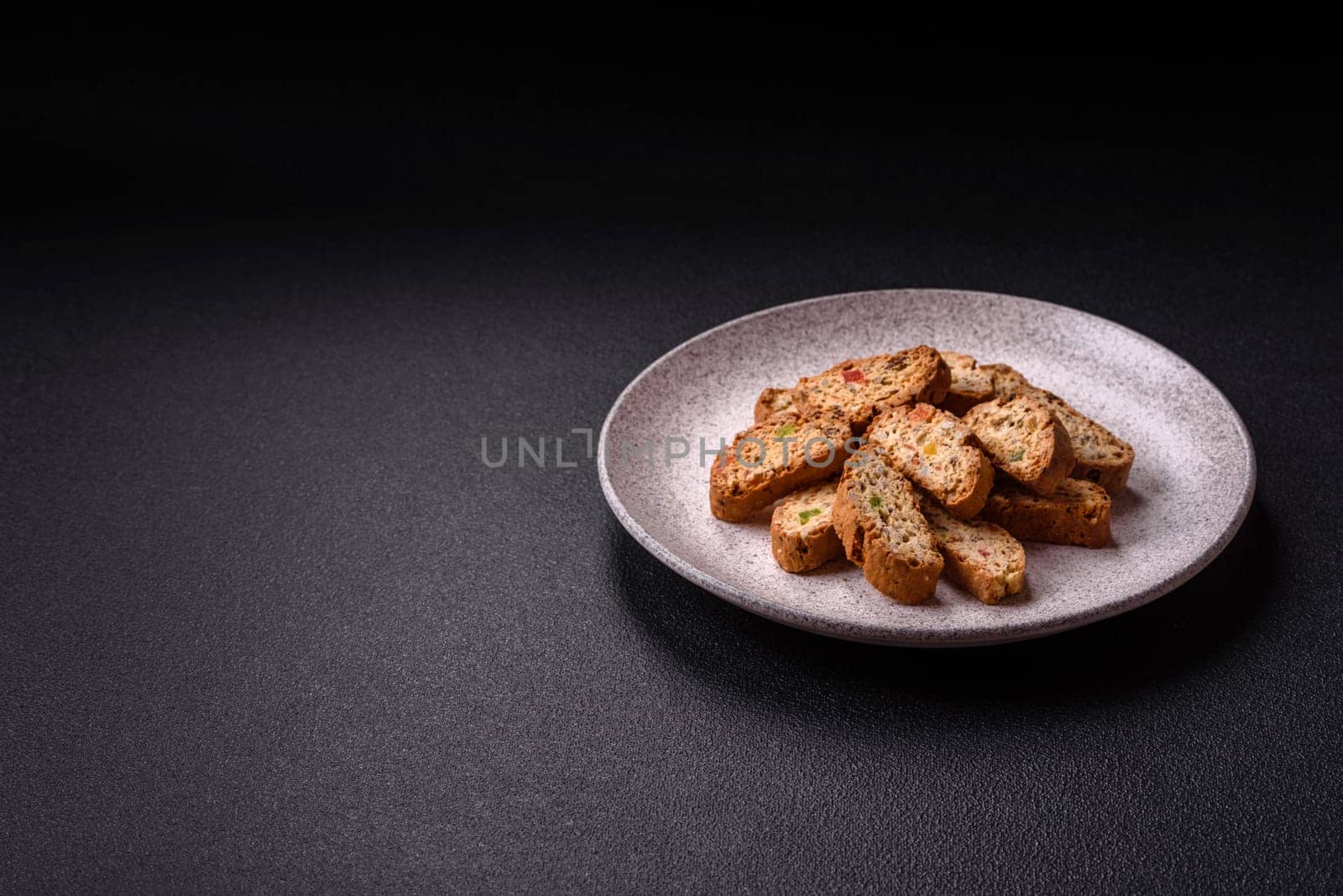 Freshly baked Italian cantuccini cookies with nuts and candied fruits on dark concrete background