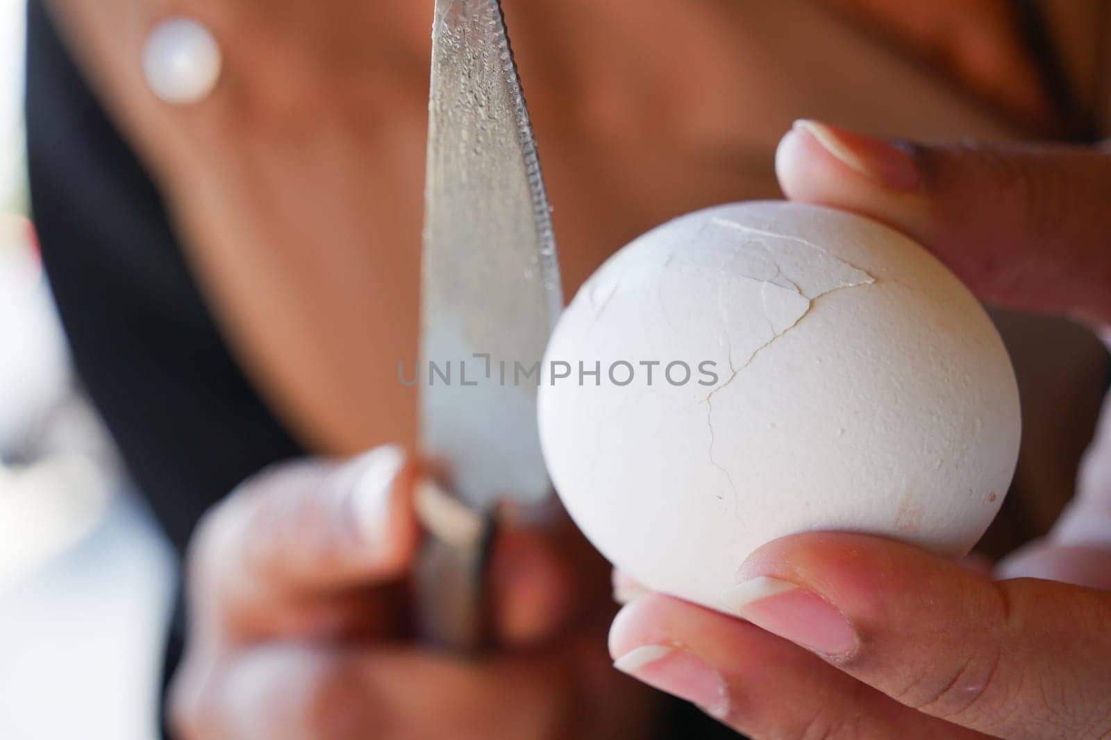 A detailed closeup shot captures a hand firmly holding a cracked egg with a knife