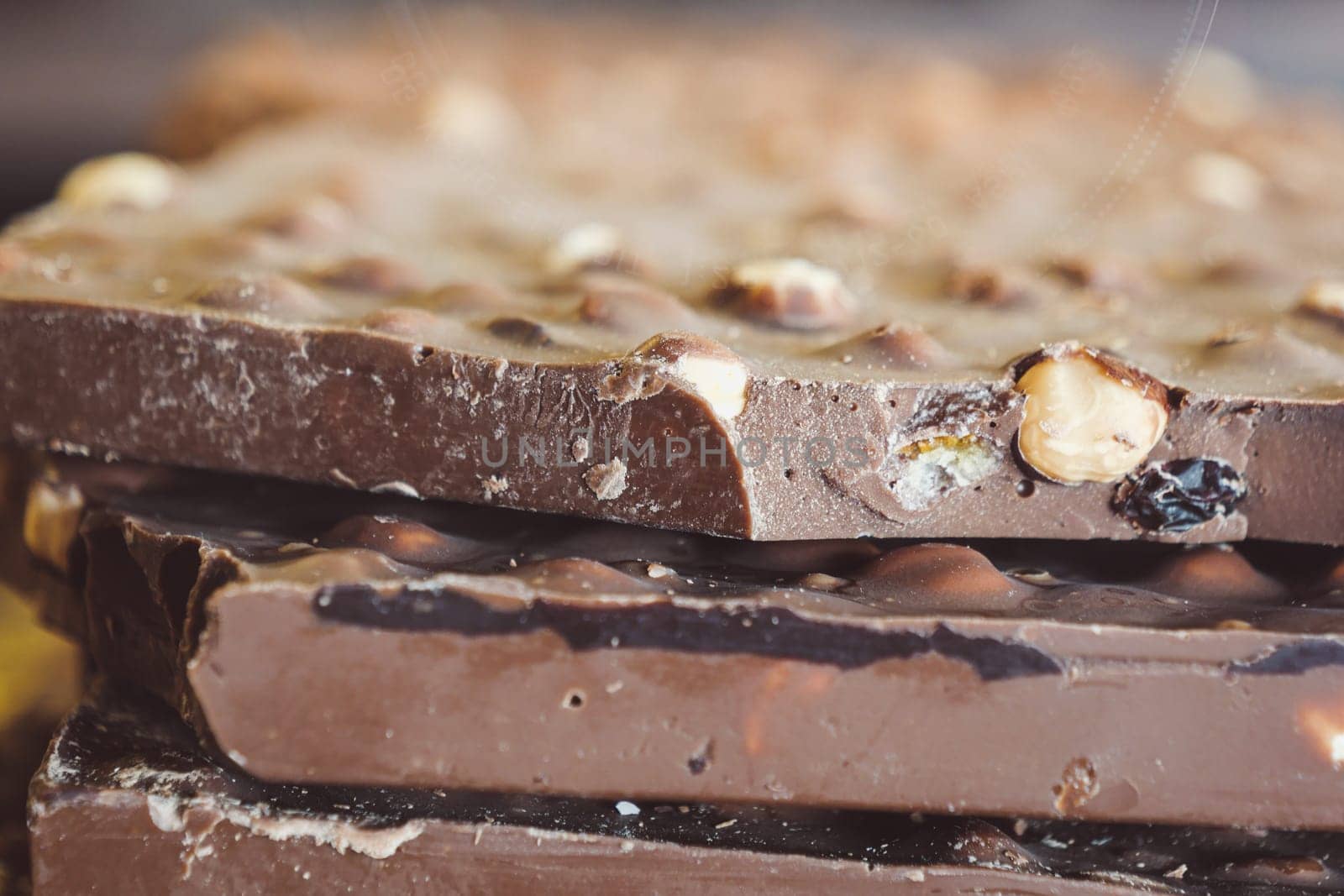 A closeup view of multiple stacked chocolate bars artfully arranged with crunchy nuts on top