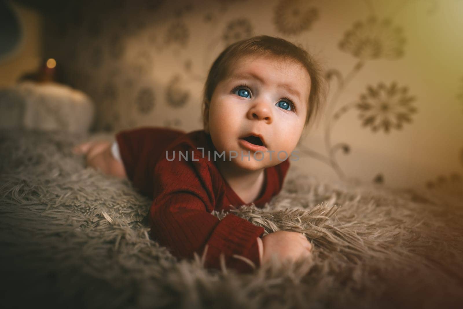 Blue-eyed baby girl in red clothes close up crawling on bed. Adorable kid portrait. 5 month old child. Childhood concept. High quality photo