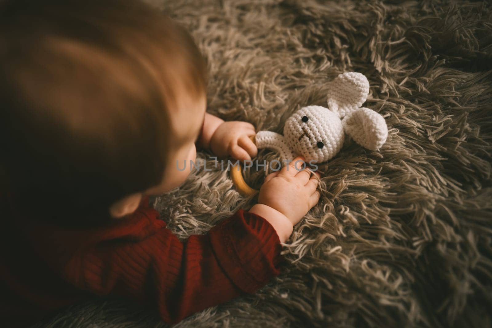 Adorable baby playing with bunny toy on fluffy brown bed coat. Babyhood and playtime concept. High quality photo