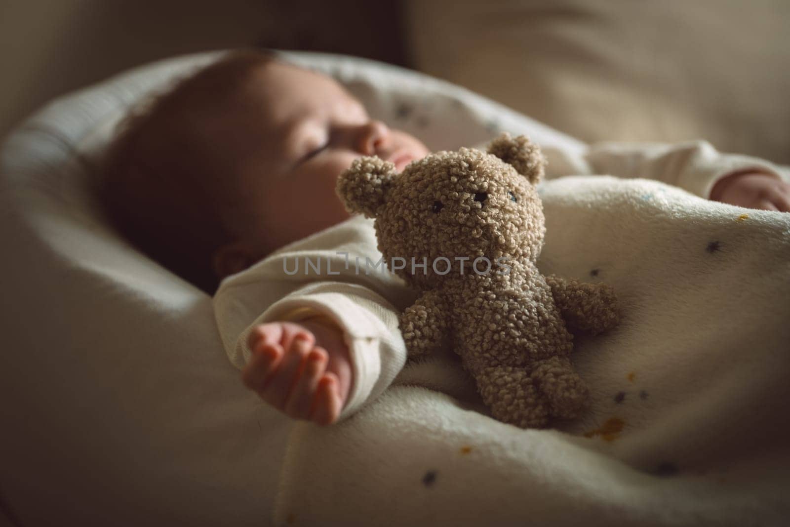 Sleeping newborn baby lying with a soft teddy bear under the blanket in warm, cozy sunlight. Childhood and parenting concept. High quality photo