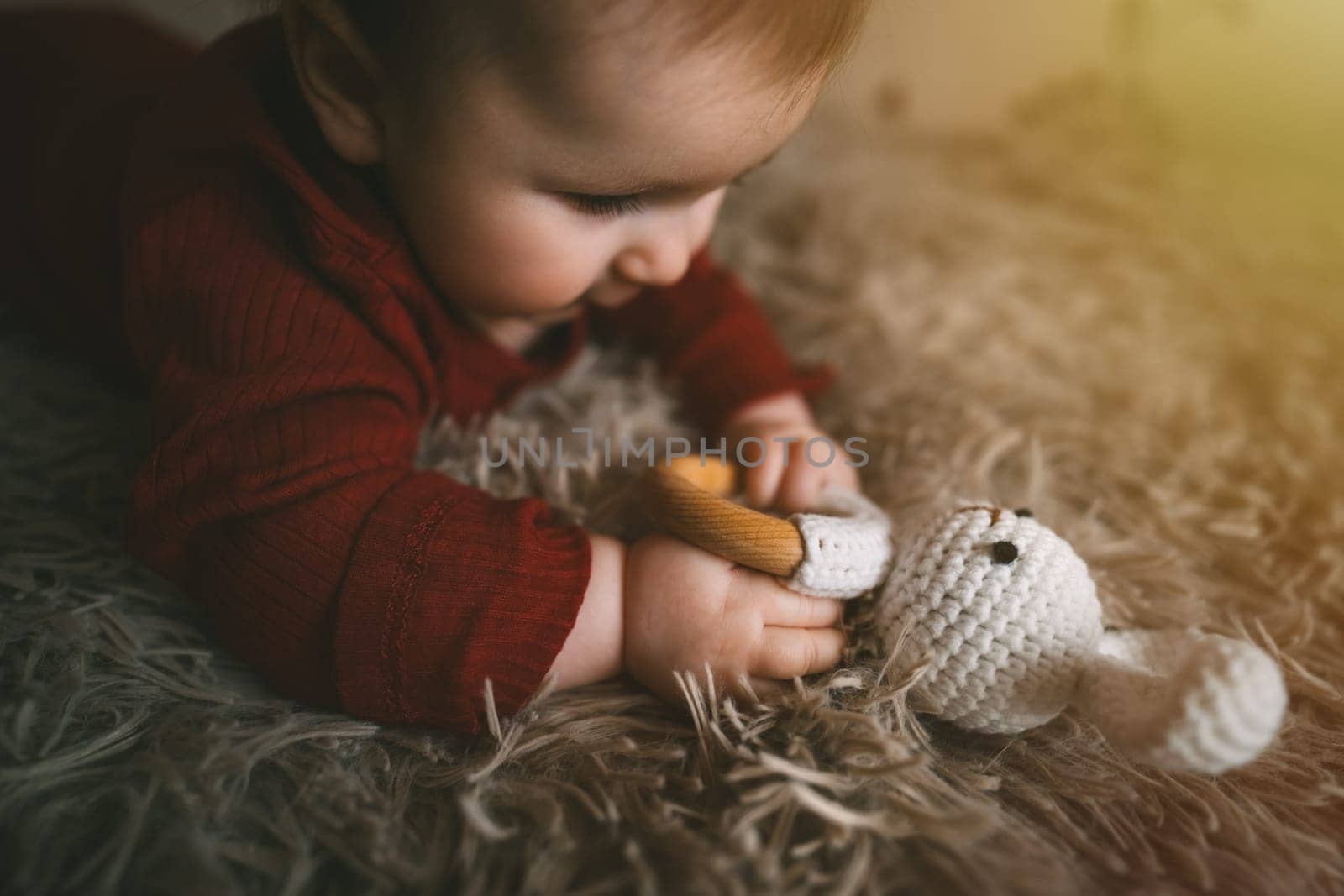 Adorable baby playing with bunny toy on fluffy brown bed coat. Babyhood and playtime concept. High quality photo