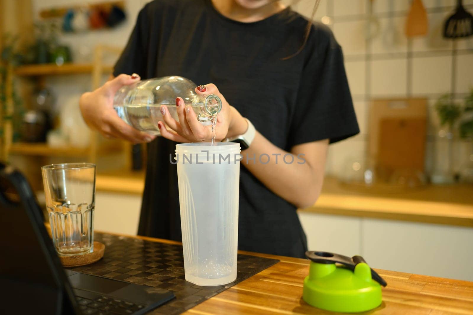 Young asian woman preparing protein shake after home workout in a kitchen.