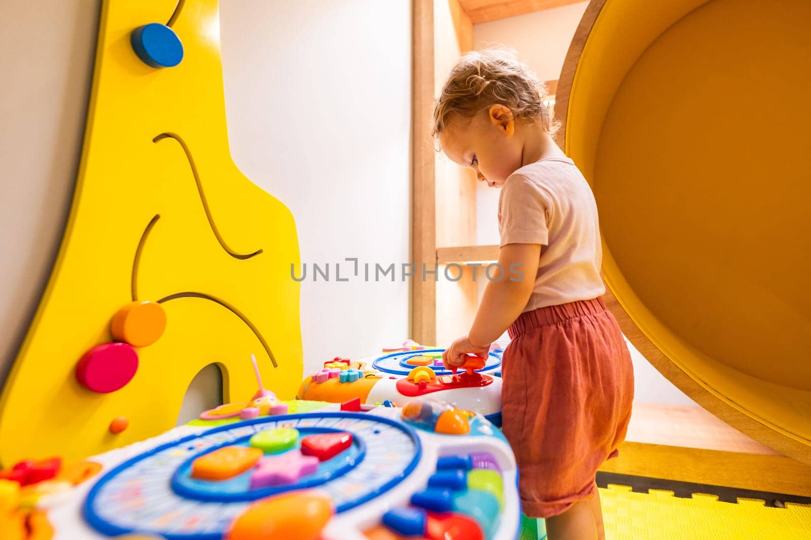 Little girl exploring activity table with buttons, shapes, and sounds in a kids' playroom