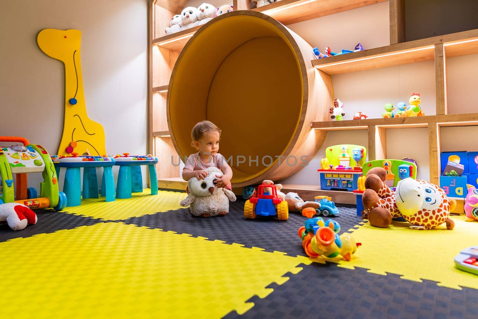 Toddler engaging with plush toy and interactive games in vibrant indoor play space
