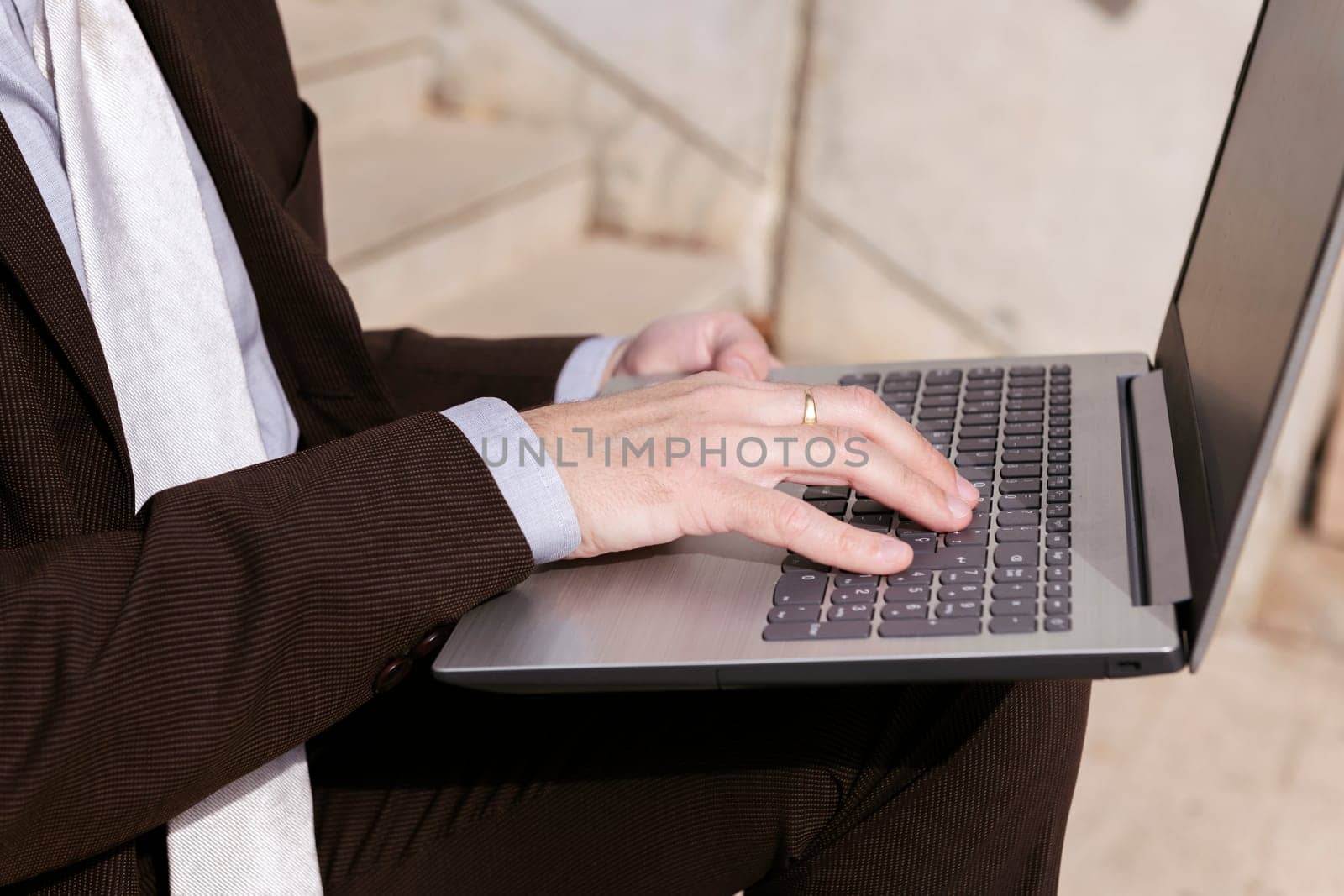 close up of the hands of an unrecognizable male entrepreneur in formal clothes sitting on urban stairway and working online on laptop in city, concept of business and remote work