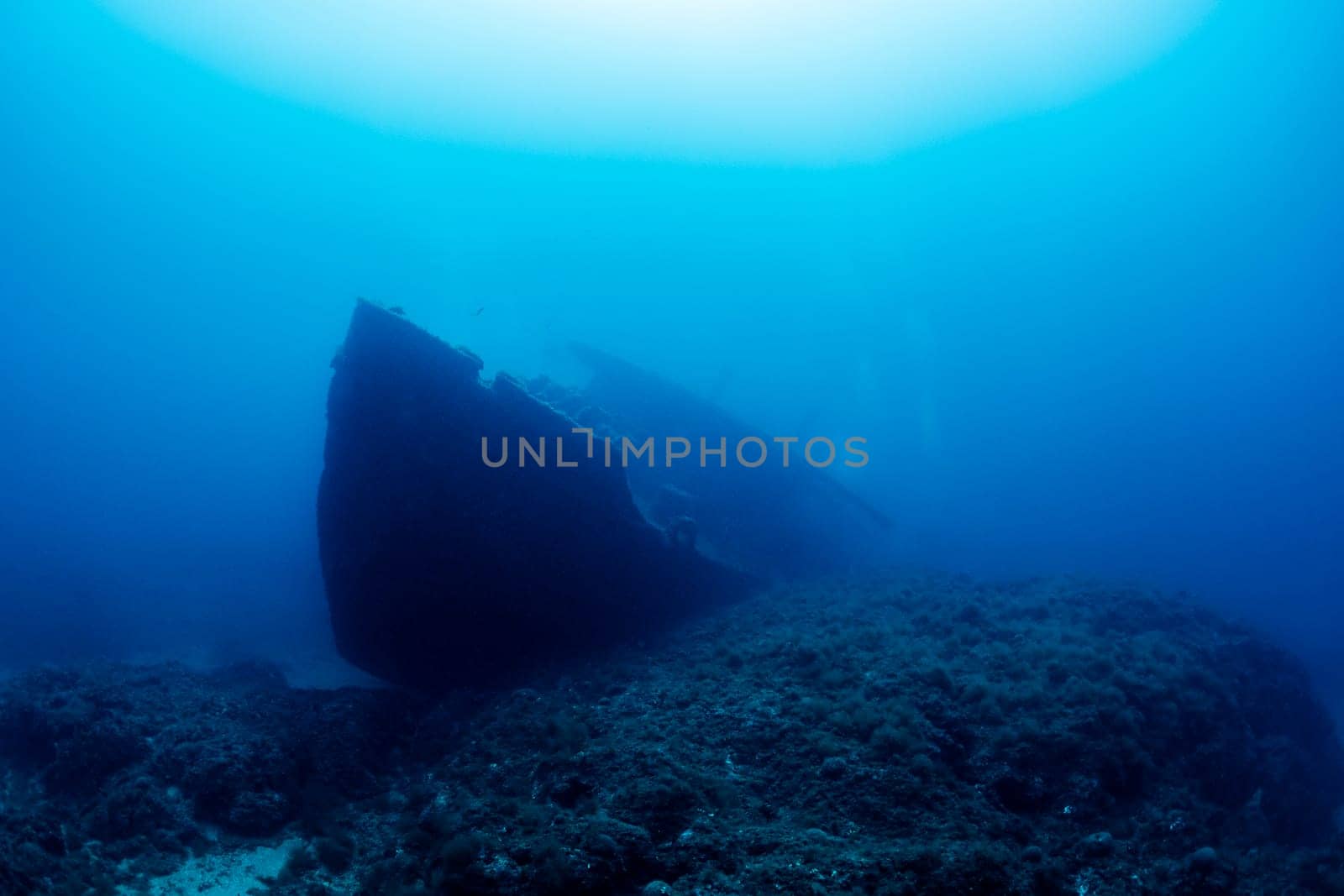 wreck of an old ruined ship on ocean rocky bottom covered with moss and algae in deep blue sea with clear water and light glare, concept of underwater adventure and seascape