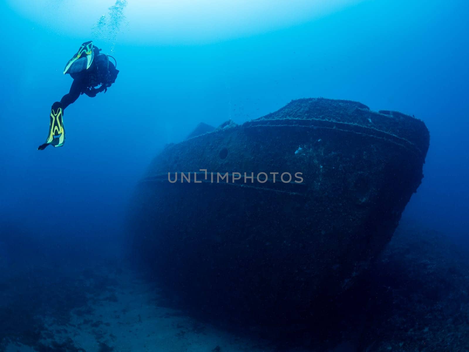 scuba diver diving near of the wreck of an old ruined ship on the bottom of deep blue sea with clear water and light glare, concept of underwater adventure and seascape
