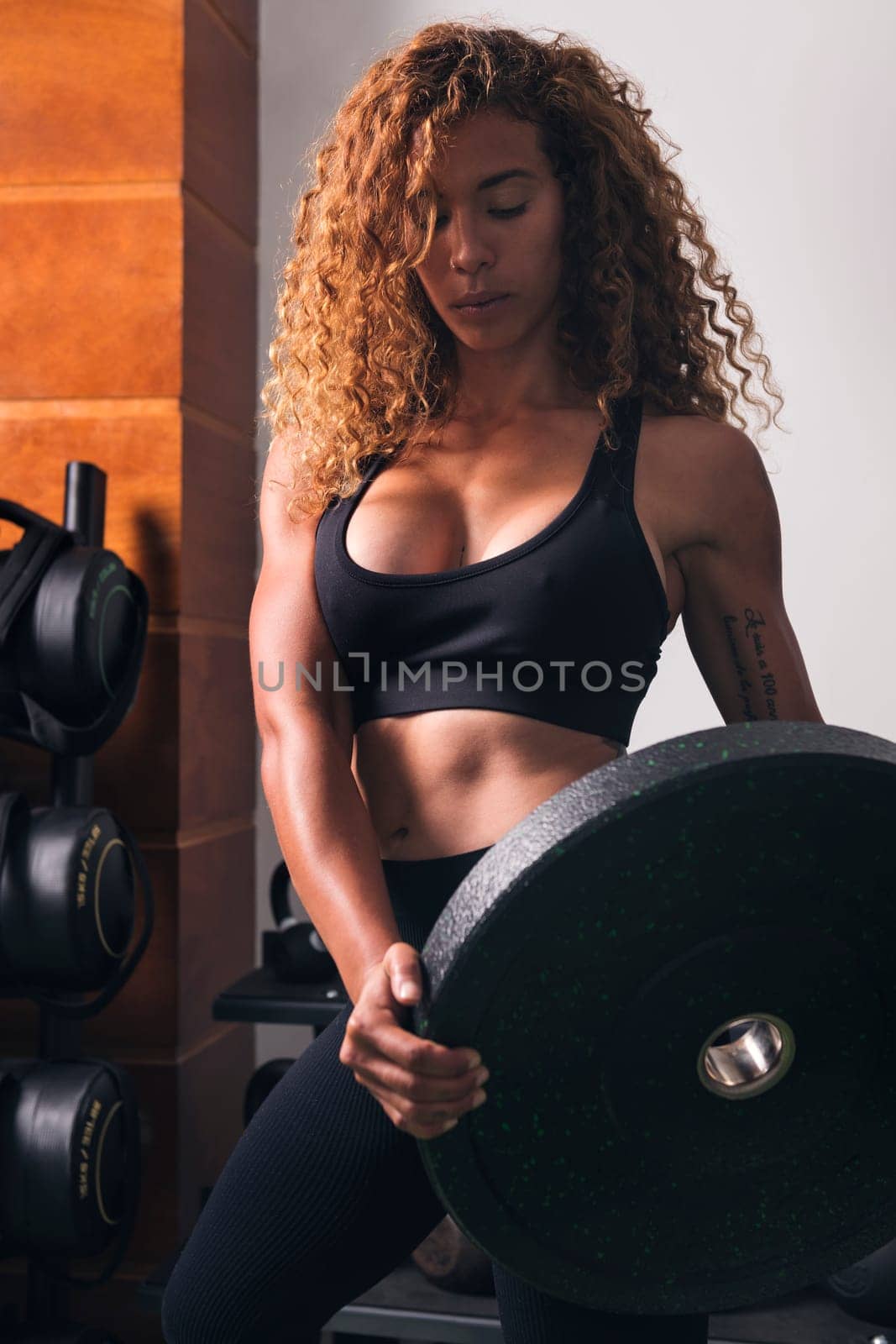 concentrated muscular sportswoman standing with heavy weight plate during workout in gym, concept of fitness and active lifestyle