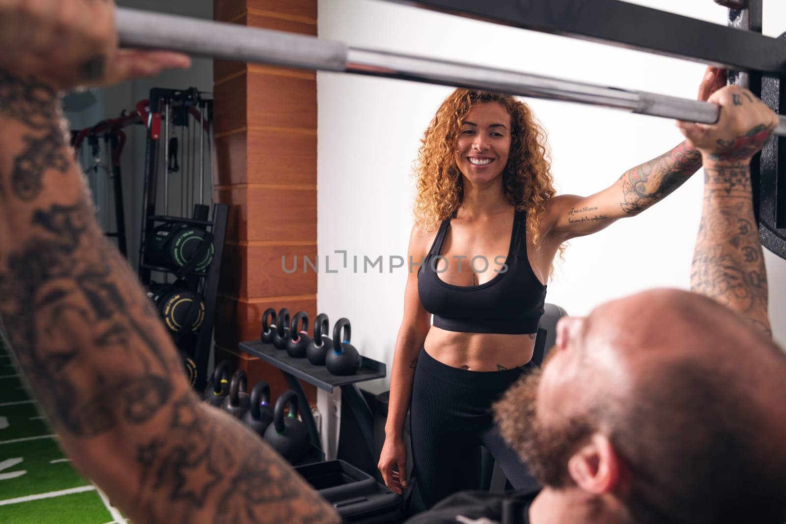 unrecognizable sportsman with tattoos lifting barbell with heavy weights during functional workout with female instructor in gym, concept of fitness and active lifestyle