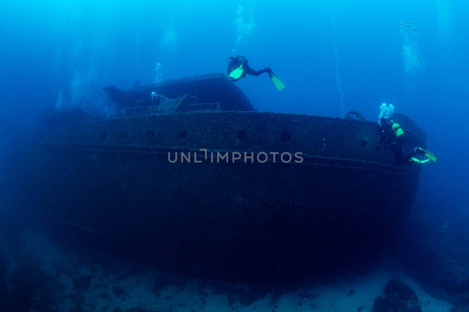 two scuba divers diving near of the wreck of an old ruined ship on the bottom of deep blue sea with clear water and light glare, concept of underwater adventure and seascape