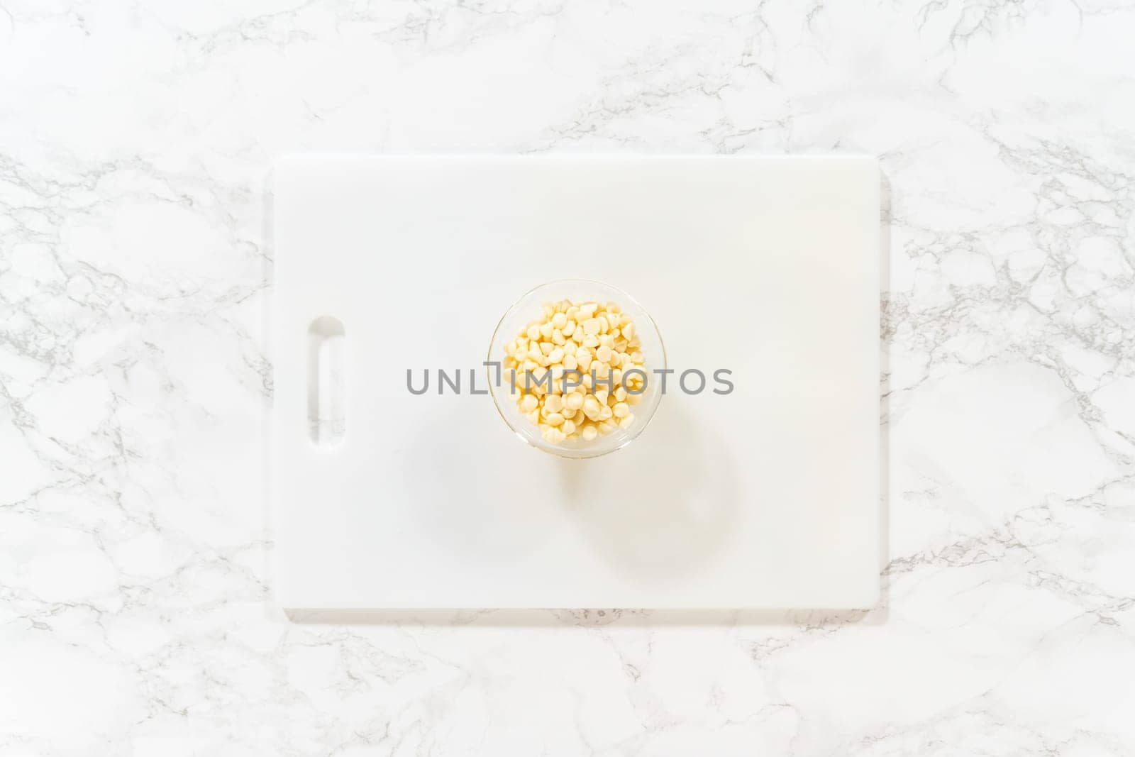 Flat lay. On a white cutting board, skillfully chopping white chocolate chips with a knife adds the perfect touch to a baking adventure.
