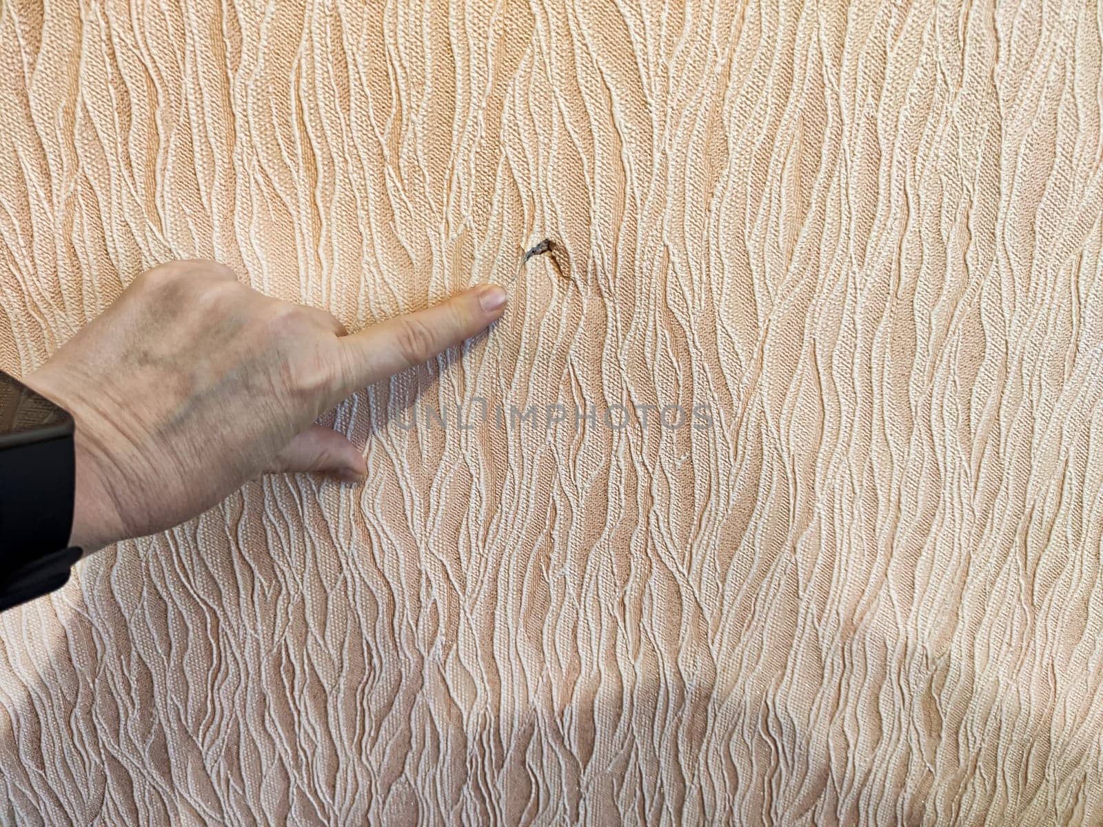 Wallpaper displays a significant tear with a hand pointing to the damage, illustrating the need for repair.