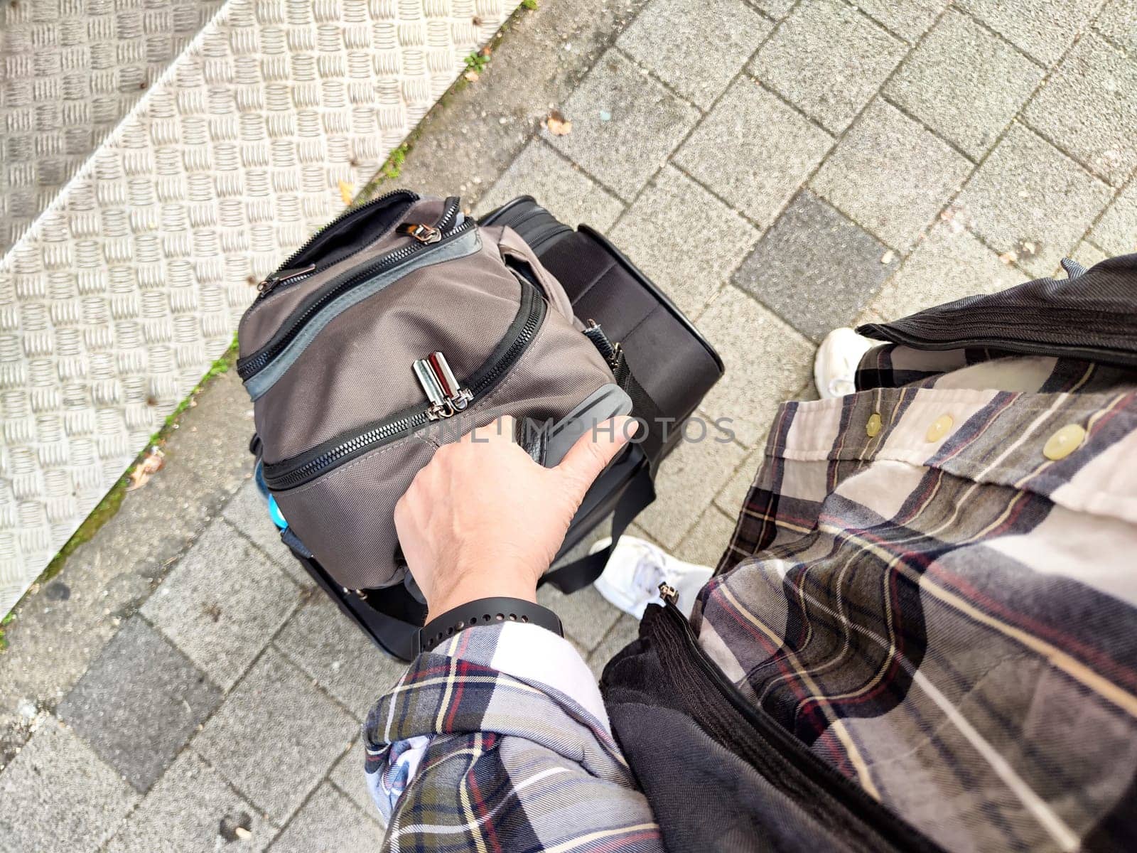 Person with a small backpack pulls a wheeled bag on a city sidewalk, capturing the essence of urban exploration in the afternoon.