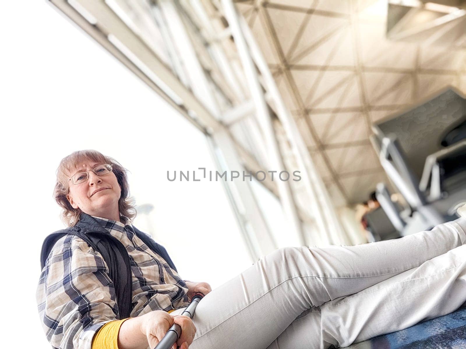 A middle-aged woman is sitting comfortably in an airport terminal, smiling as she takes a selfie with a relaxed demeanor.