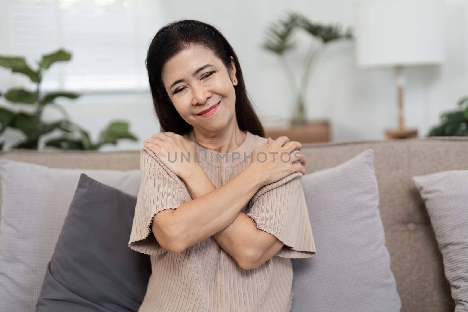 A woman hugging herself, representing self-protection and inner strength, seated in a cozy, modern living room.