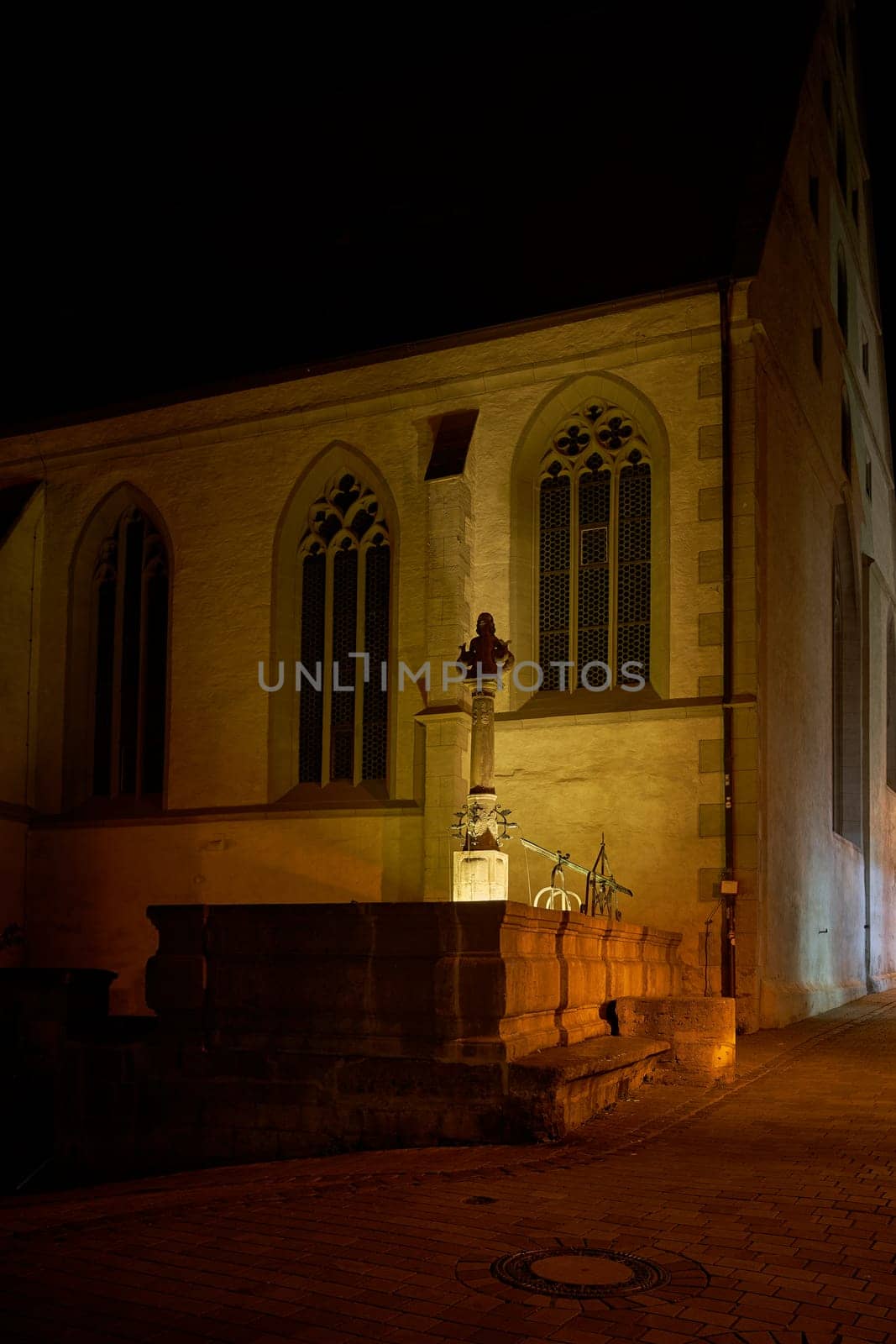Night scene at the medieval Johannisbrunnen fountain in front of St. Johannis in the old town of Rothenburg ob der Tauber in Germany