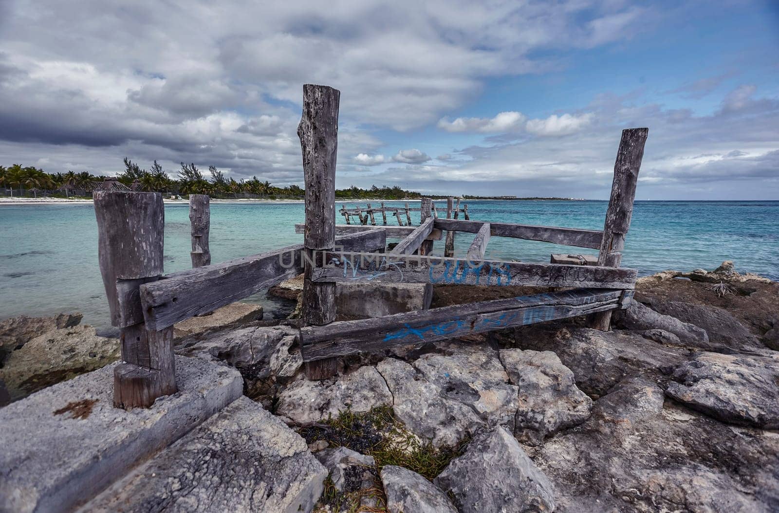 Decaying wooden pier structure sinking into the rocky shore of xpu-ha beach in riviera maya, mexico, under cloudy sky