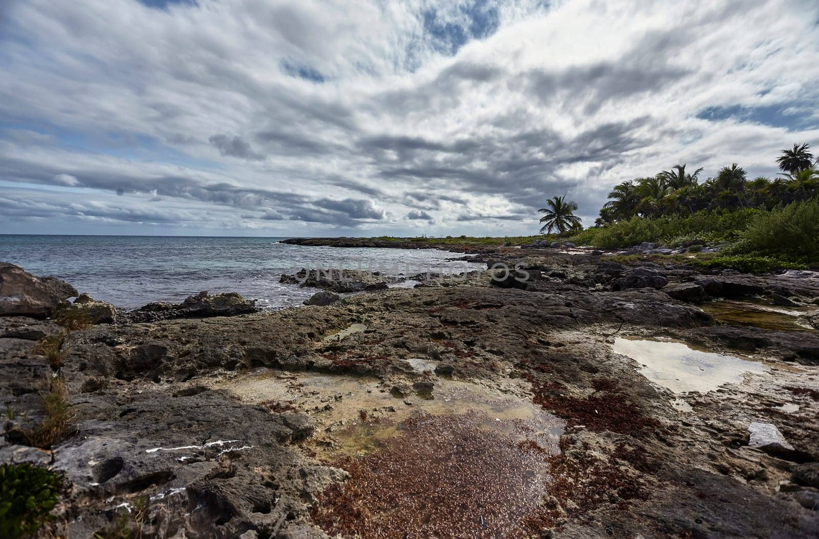Breathtaking scenery of the rocky coastline in xpu-ha, mexico, where the turquoise waters meet the shore under a cloudy sky