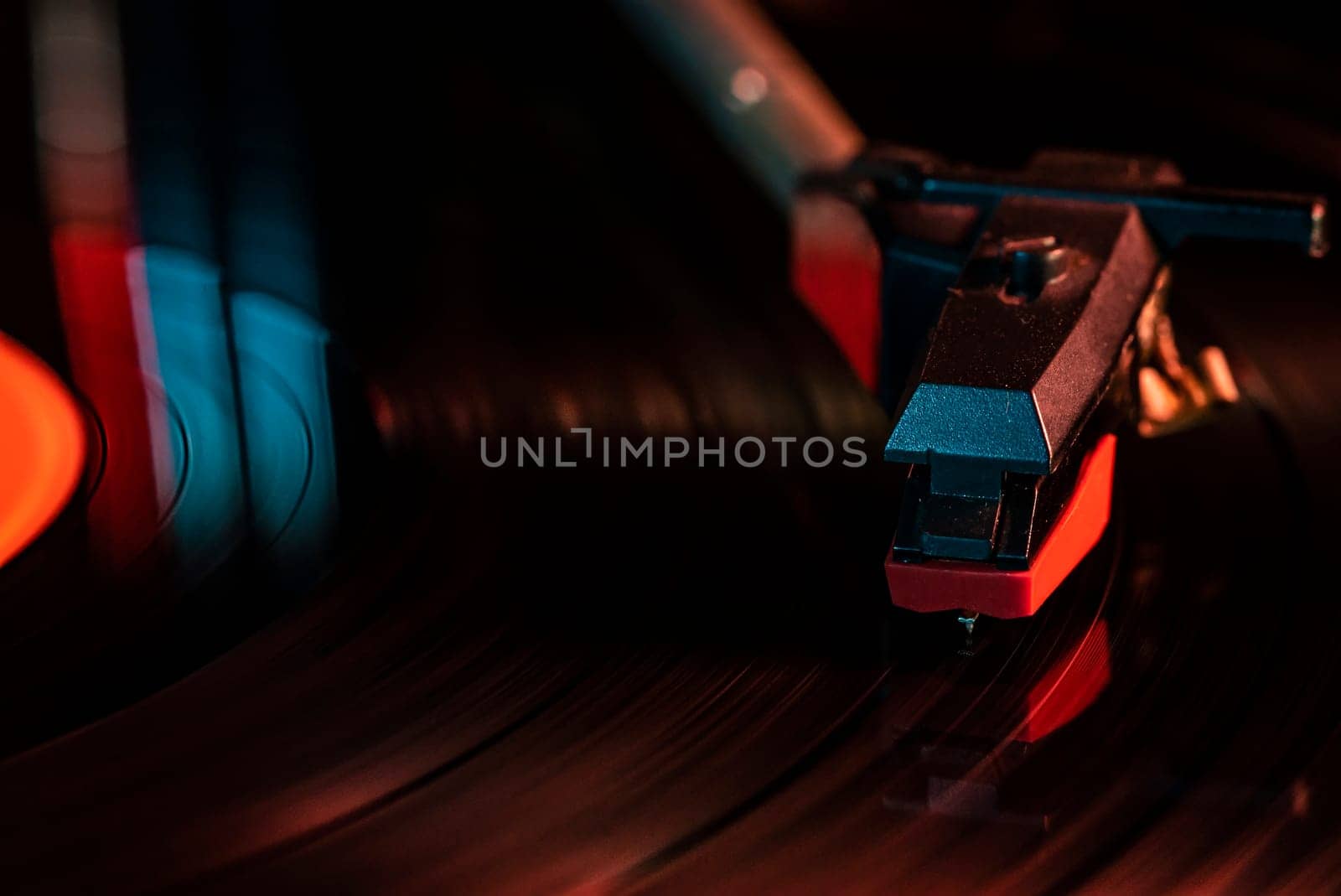 Close-up of a record player needle reading a spinning vinyl record, illuminated by colorful lights