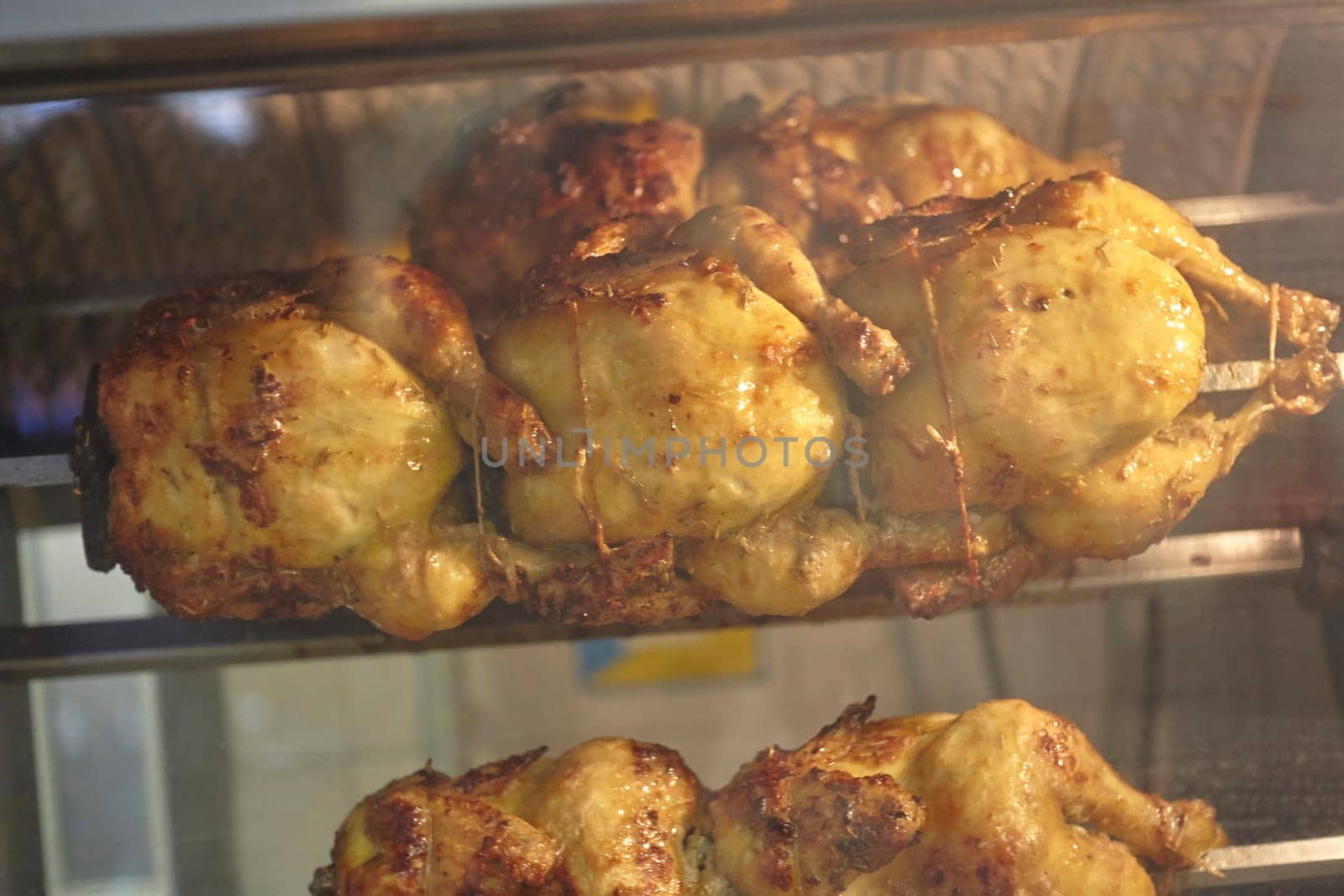 Delicious rotisserie chicken cooking on a spit in a commercial oven, rotating slowly and becoming golden brown