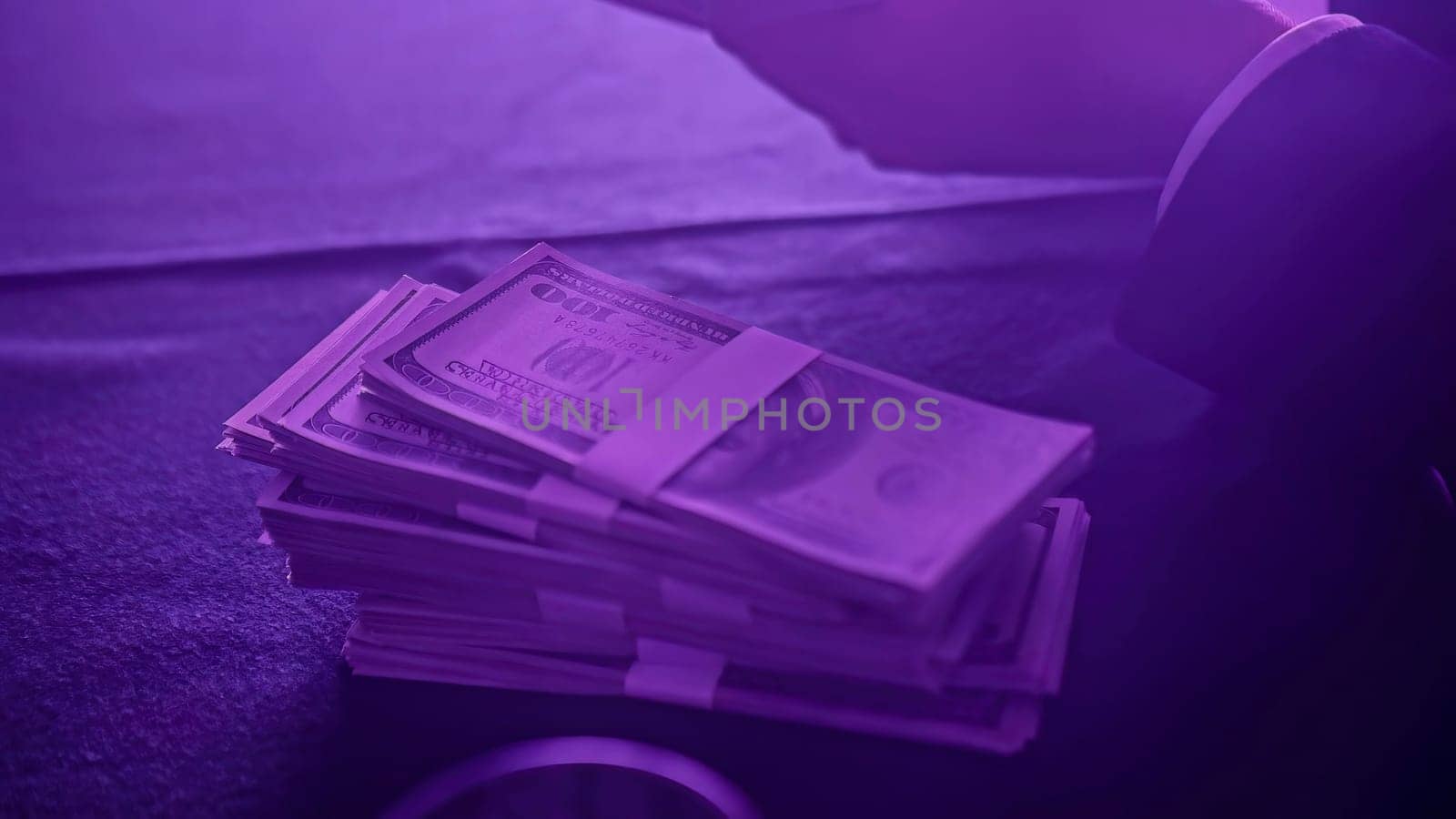 Businessman counting large stacks of one hundred dollar bills under purple light