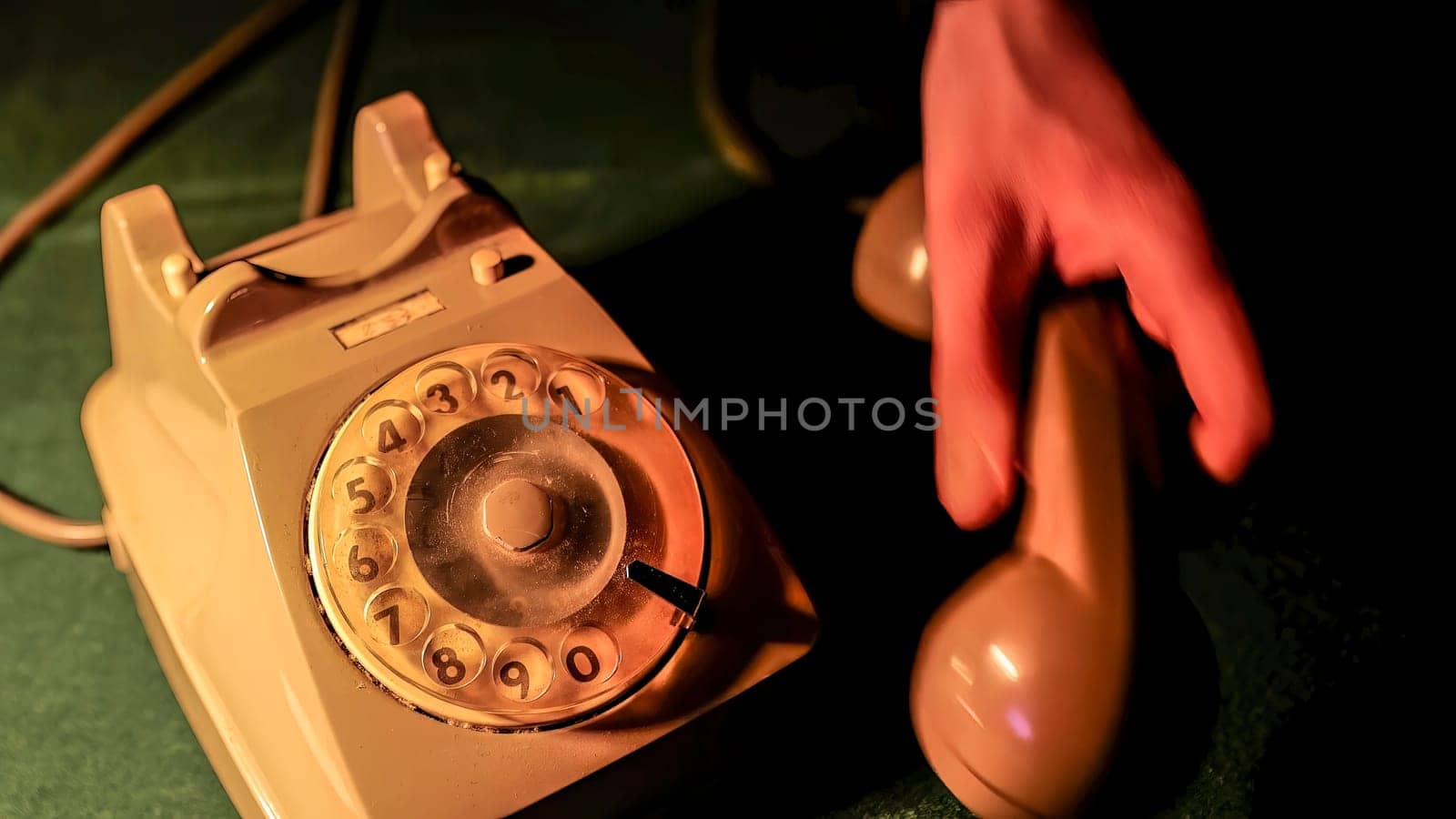 Close-up of hand picking up the receiver of an old rotary phone, illuminated by dramatic lighting, evoking a sense of mystery and nostalgia
