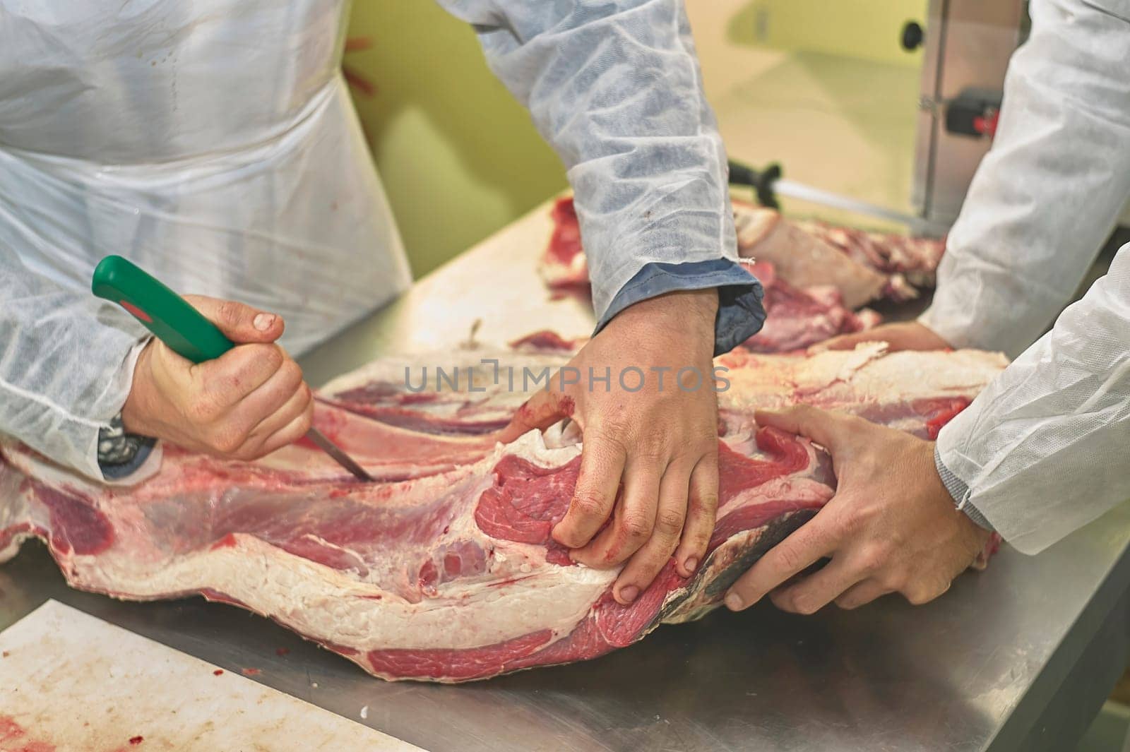 Butchers are processing beef carcass using knives in a meat factory