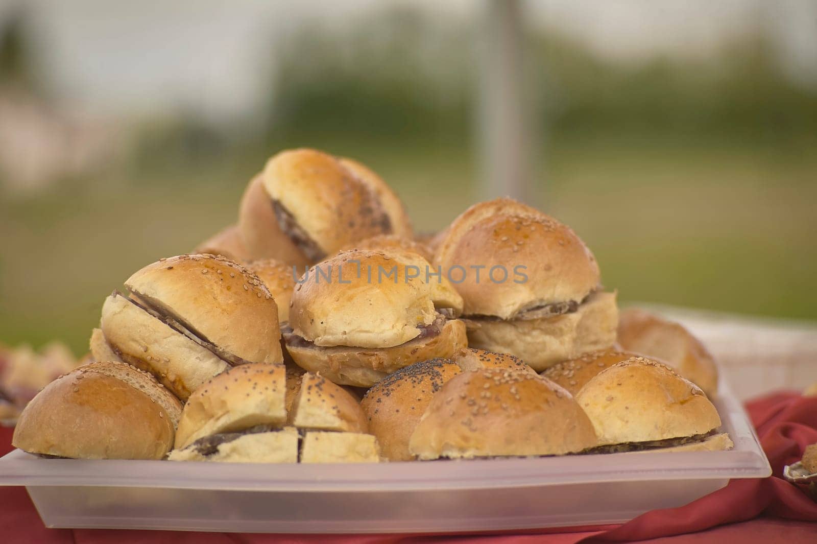 Delicious mini burgers topped with poppy and sesame seeds are neatly arranged on a plastic tray, ready to be served