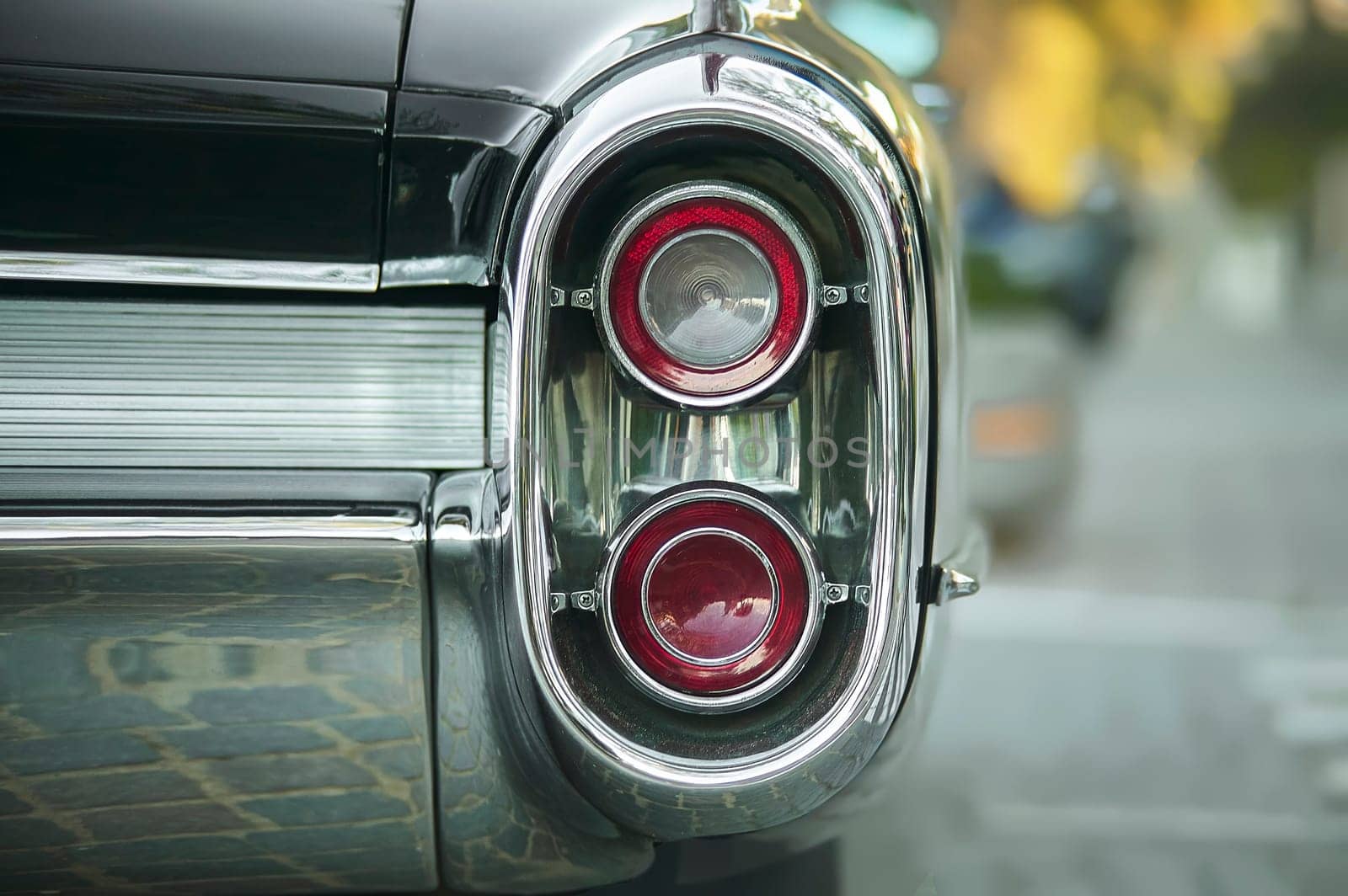 Close-up of vintage car's taillights showcasing its chrome details and reflecting urban surroundings