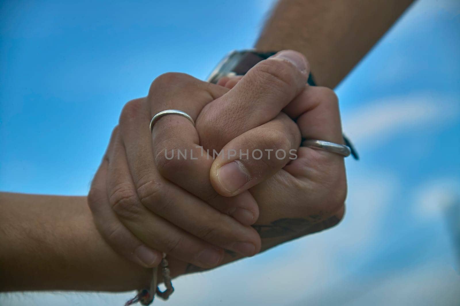 Couple holding hands showing rings under blue sky, celebrating their love and commitment