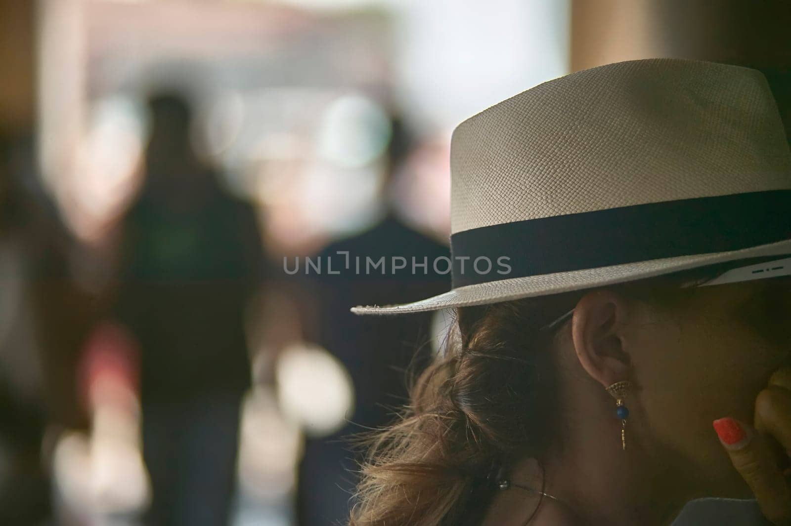 Stylish woman wearing panama hat standing in a blurred crowd, enjoying a casual outing