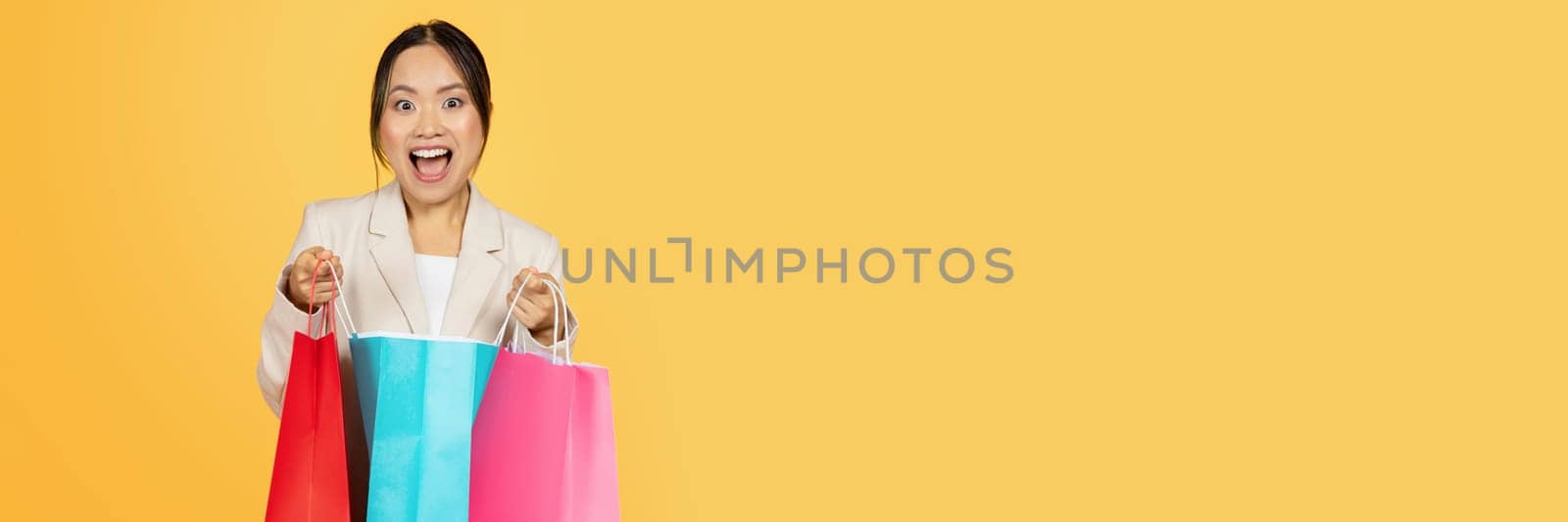 Surprised glad young japanese lady shopaholic open colorful bags, with purchases enjoy shopping, isolated on orange studio background. Huge sale, lifestyle and new fashion
