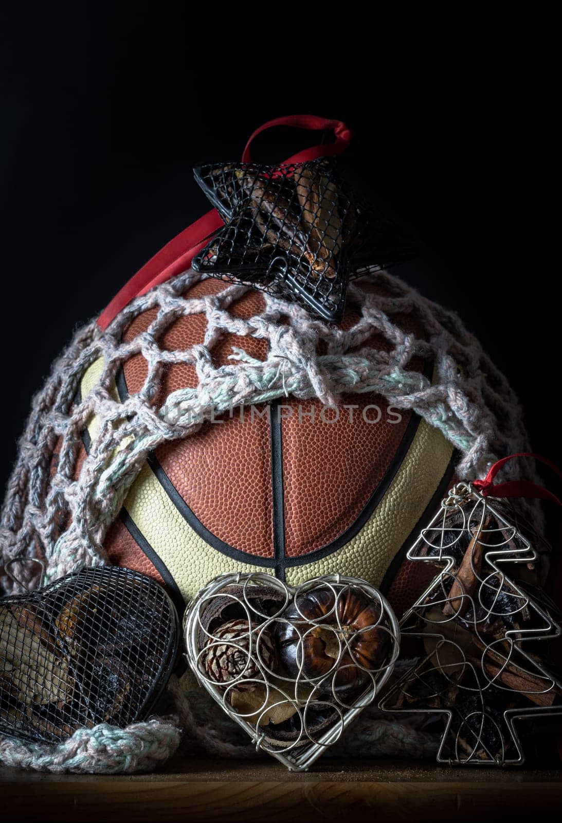 Basketball ball inside of mesh net string decoration with Christmas tree mesh case, Heart mesh case and Star mesh case on Dark background. Christmas-themed event basketball idea, sports play on christmas, use it as your Wallpaper, Poster and Space for text, Selective focus.