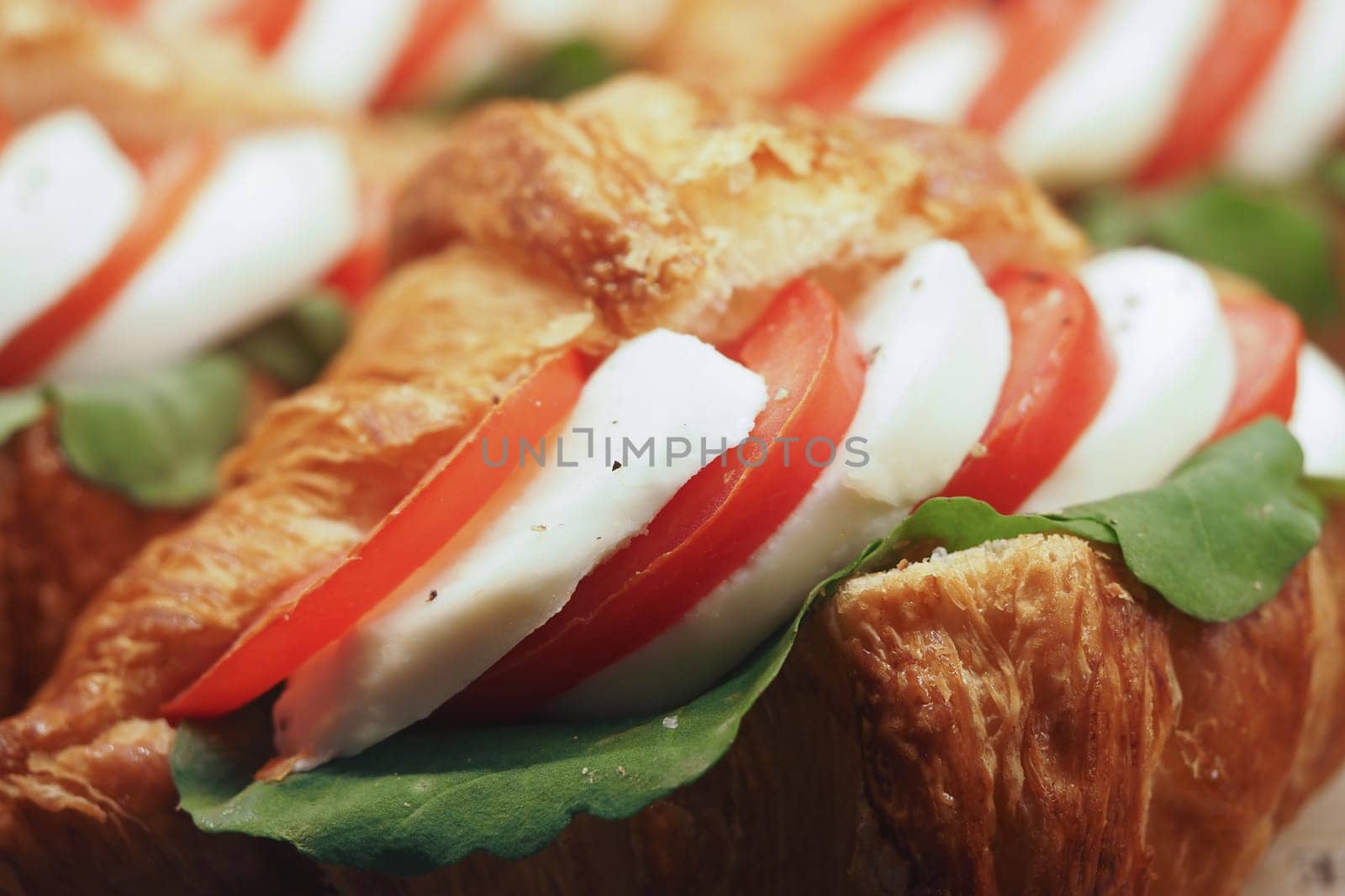 A tasty croissant filled with juicy tomato, rich mozzarella cheese, and fresh greens