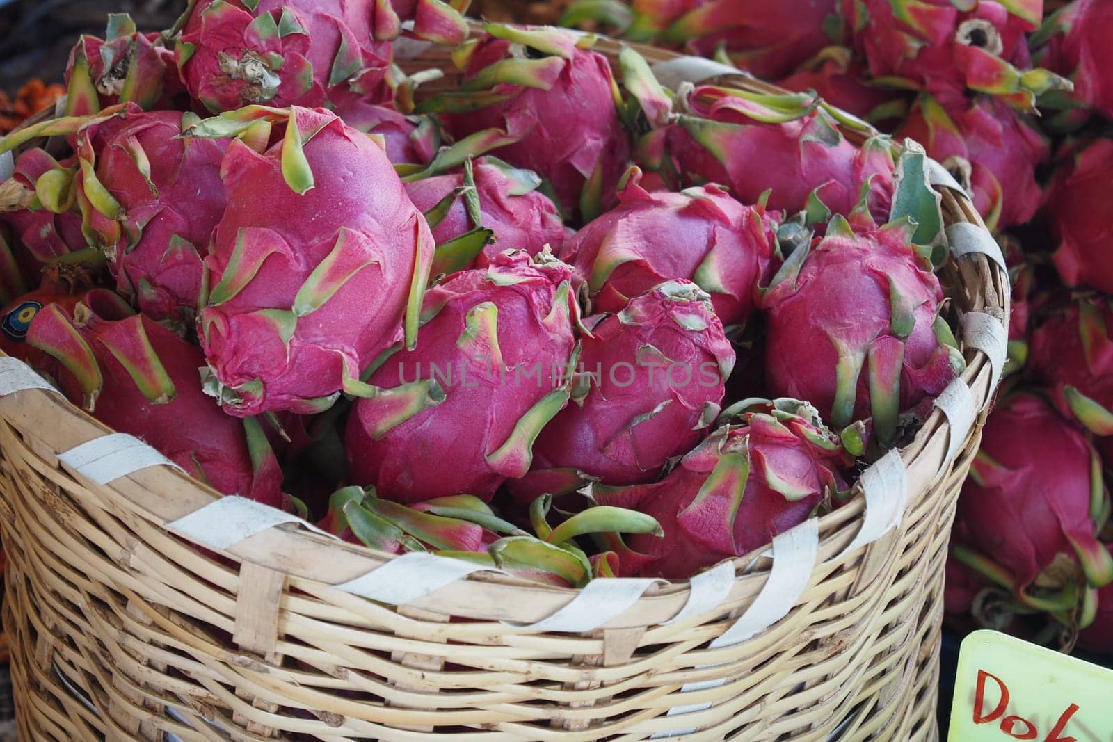 Colorful dragon fruits are beautifully displayed in a woven basket at a lively market