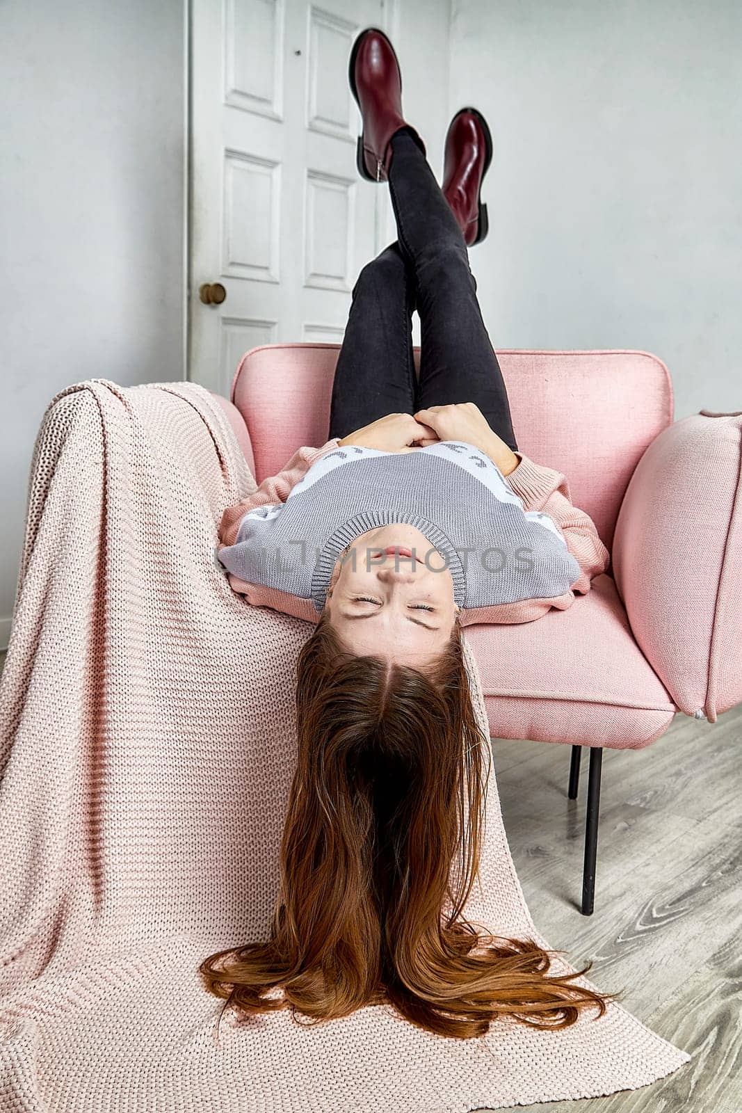 Trendy model lies upside down on a pink sofa, displaying a unique fashion choice with stylish shoes in a modern indoor space.