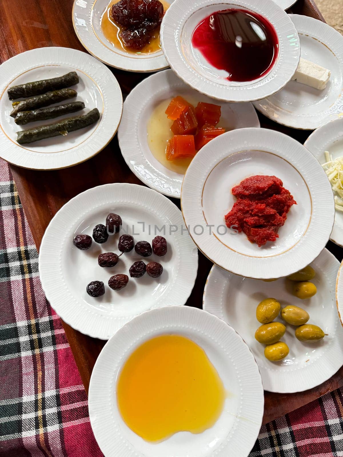 Assorted Turkish breakfast dishes with olive oil, honey, jams, rolled grape leaves, olives, feta cheese, and tomato sauce on white plates, traditional patterned tablecloth. Top view. High quality photo