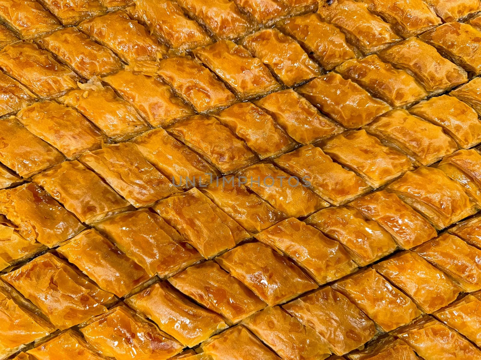 Solid background of freshly baked baklava laid out in rows, golden brown with syrup glaze, traditional Middle Eastern sweet pastry dessert, close up texture. Ramadan concept. High quality photo