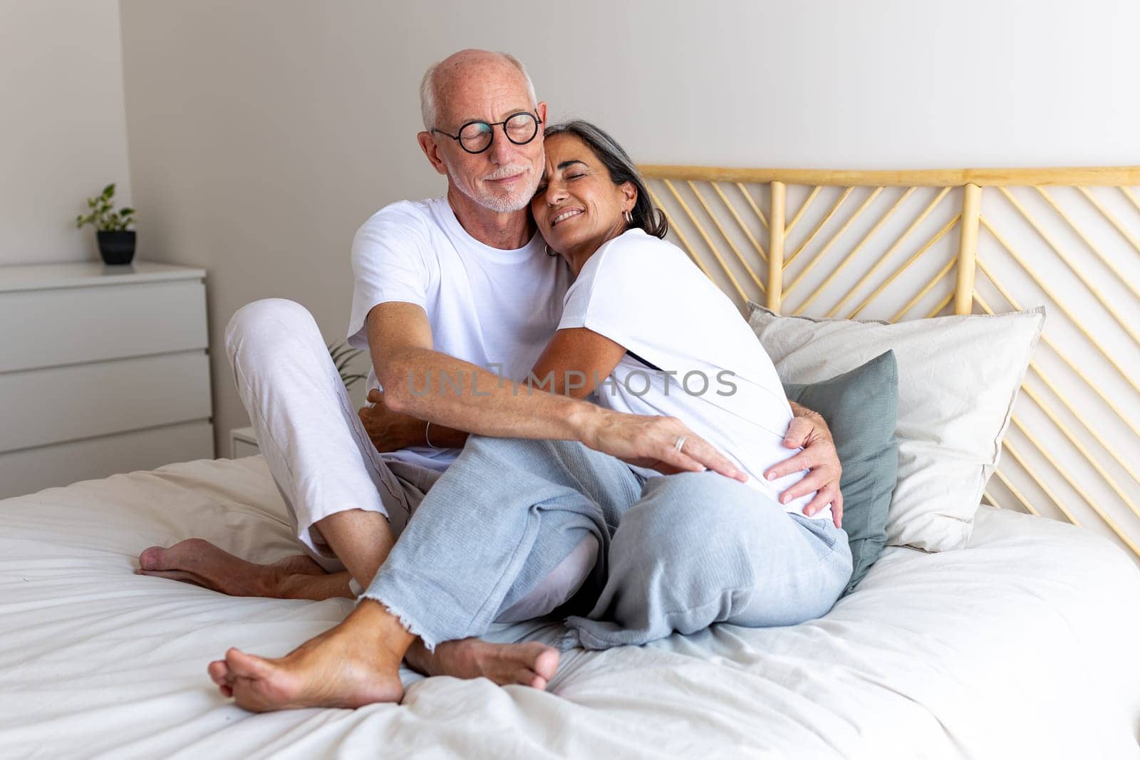 Happy mature couple embracing, relaxing together on bed. Eyes closed. Feeling connection and love. Heterosexual couple concept.