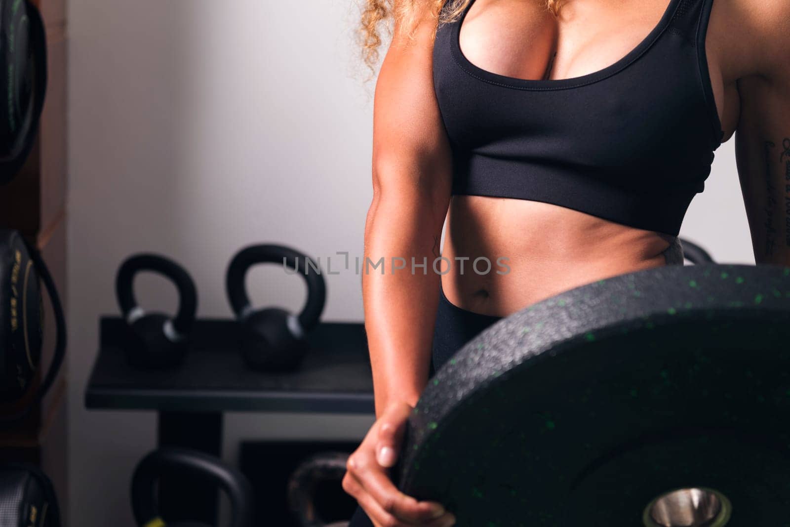 crop of unrecognizable muscular sportswoman standing with heavy weight plate during workout in gym, concept of fitness and active lifestyle