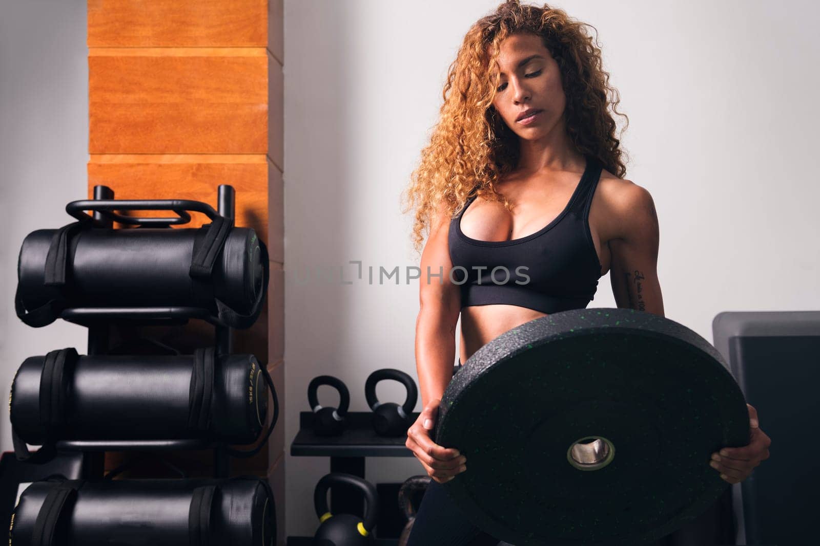 concentrated muscular sportswoman standing with heavy weight plate during workout in gym, concept of fitness and active lifestyle
