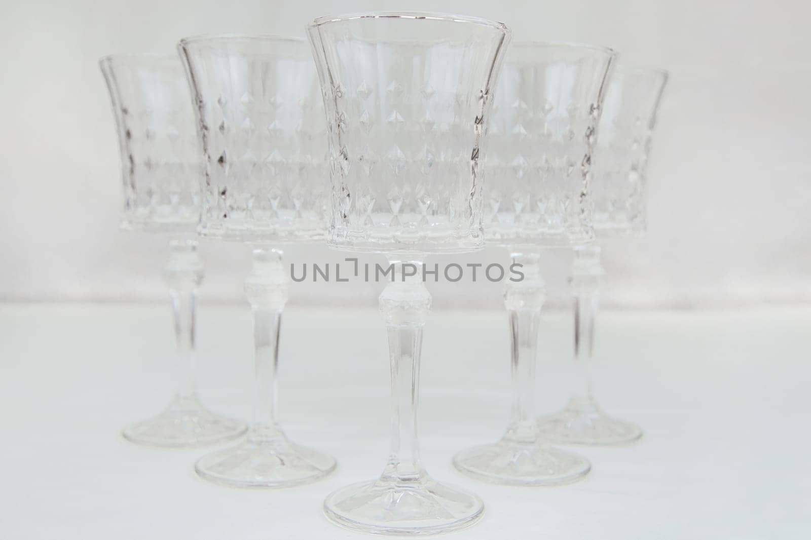 Crystal wine glasses with expanded edges and faceted pattern stand in a wedge on a white background. High quality photo