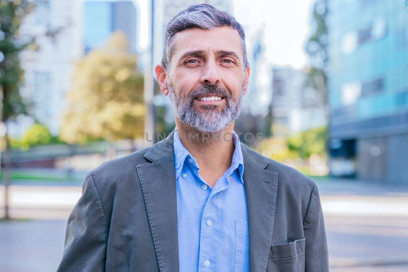 Portrait of a smiling middle-aged businessman in a smart casual outfit standing outdoors in a modern urban environment, exuding confidence and professionalism.