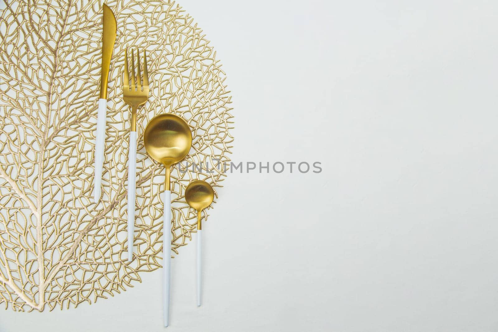 The food utensils, gold with a white handle, lie on a gold napkin on a white background. The concept of eating, the concept of serving. High quality photo