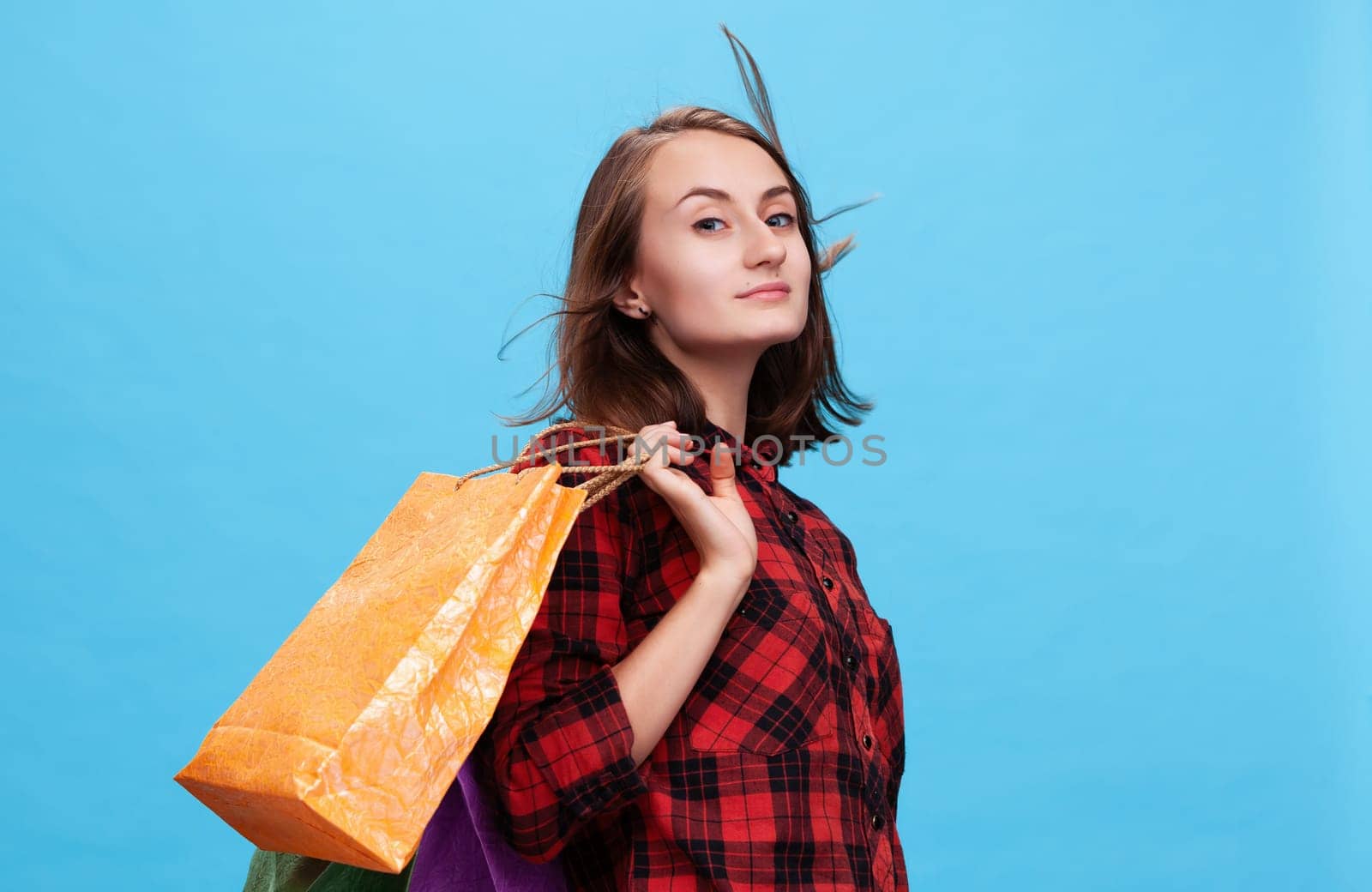 A young woman confidently poses with vibrant shopping bags against a bright blue background. She embodies the excitement of the shopping season, perfect for fashion enthusiasts.